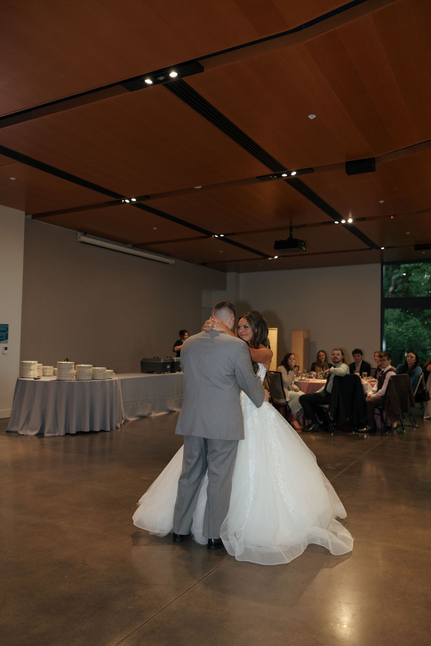 Bride and groom share their first dance at wedding reception with guests seated at tables in elegant venue.