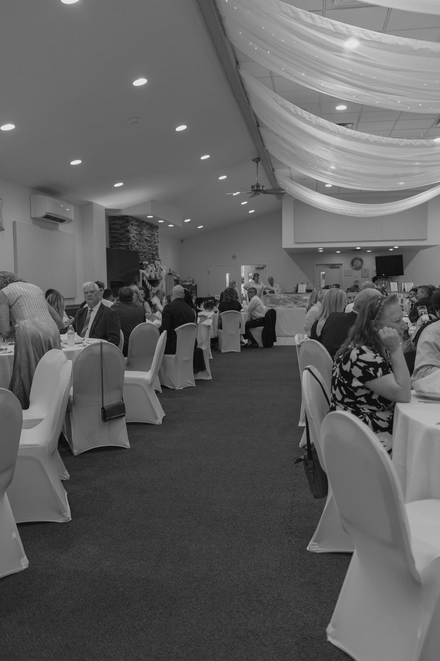 Elegant wedding reception hall in black and white with guests seated at round tables under draped ceiling.