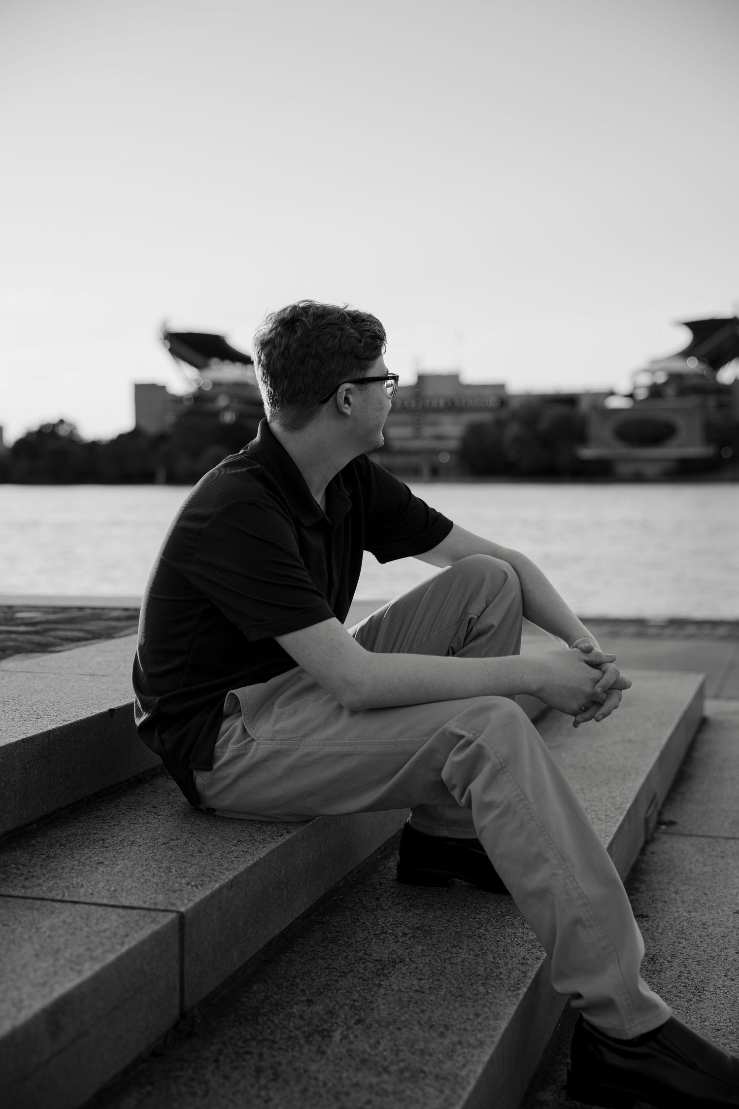 Black and white photo of teen boy sitting on steps by river.