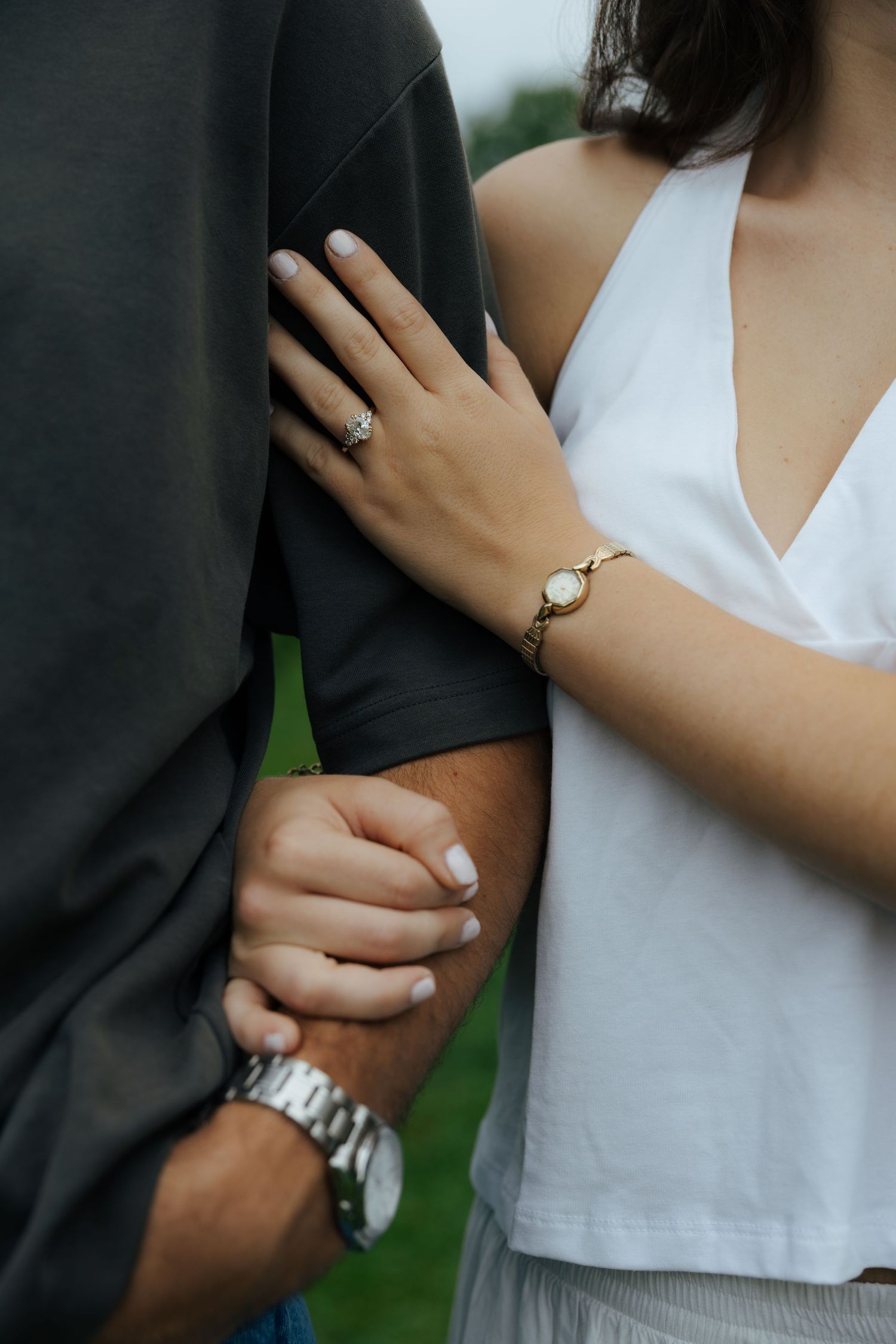 Close-up of engaged couple holding hands, woman wearing diamond ring and gold watch, man wearing silver watch.