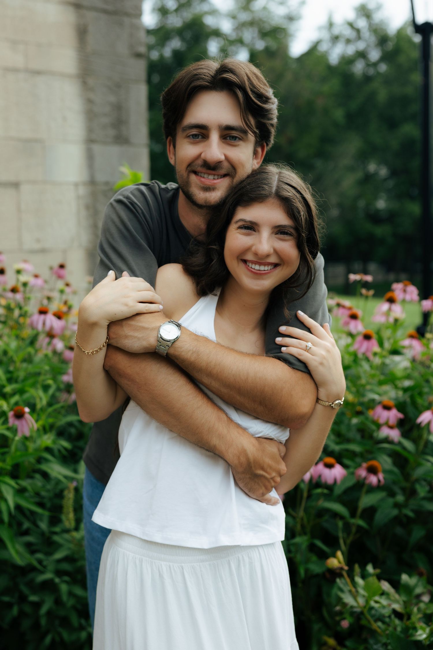 A happy couple embraces in front of pink coneflowers in a lush garden setting.