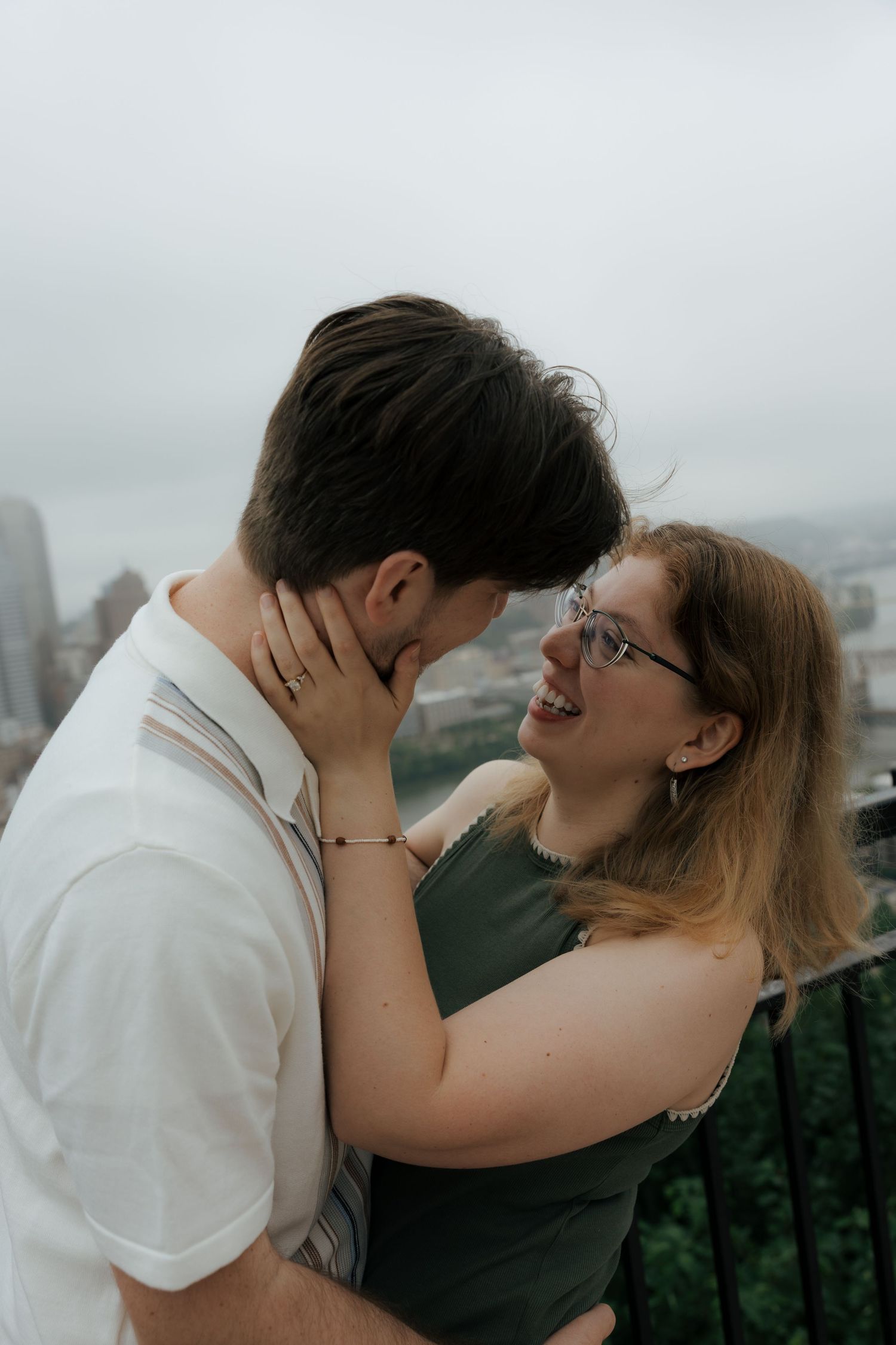 Happy woman in glasses laughing while embracing her partner with a city view behind them.