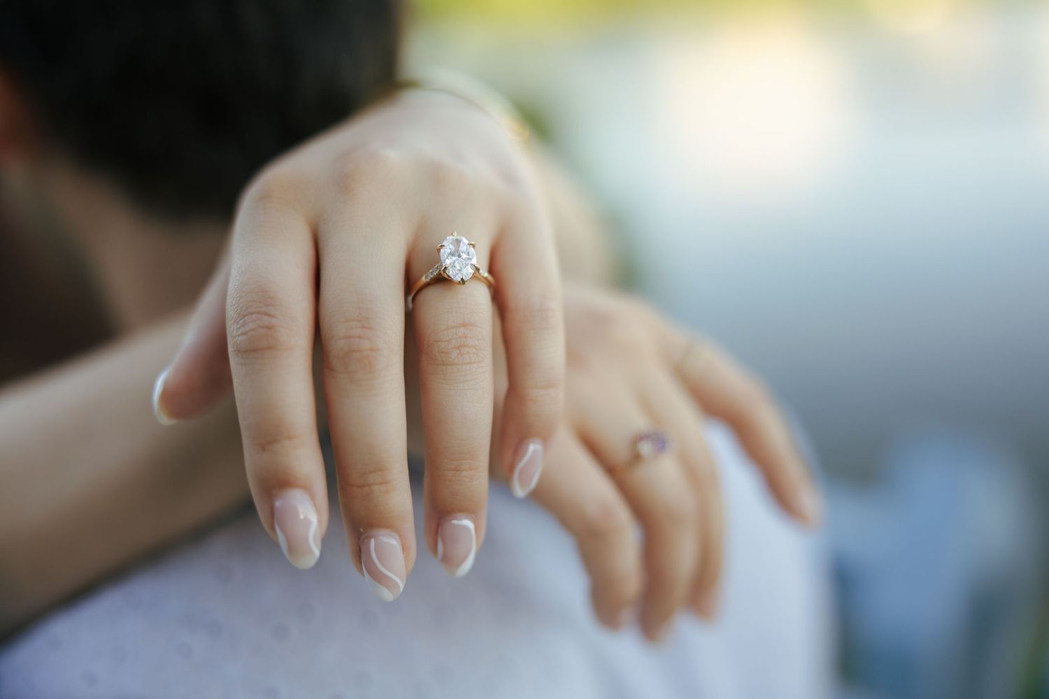 Close-up of a woman's hand displaying a sparkling diamond engagement ring while embracing her partner.