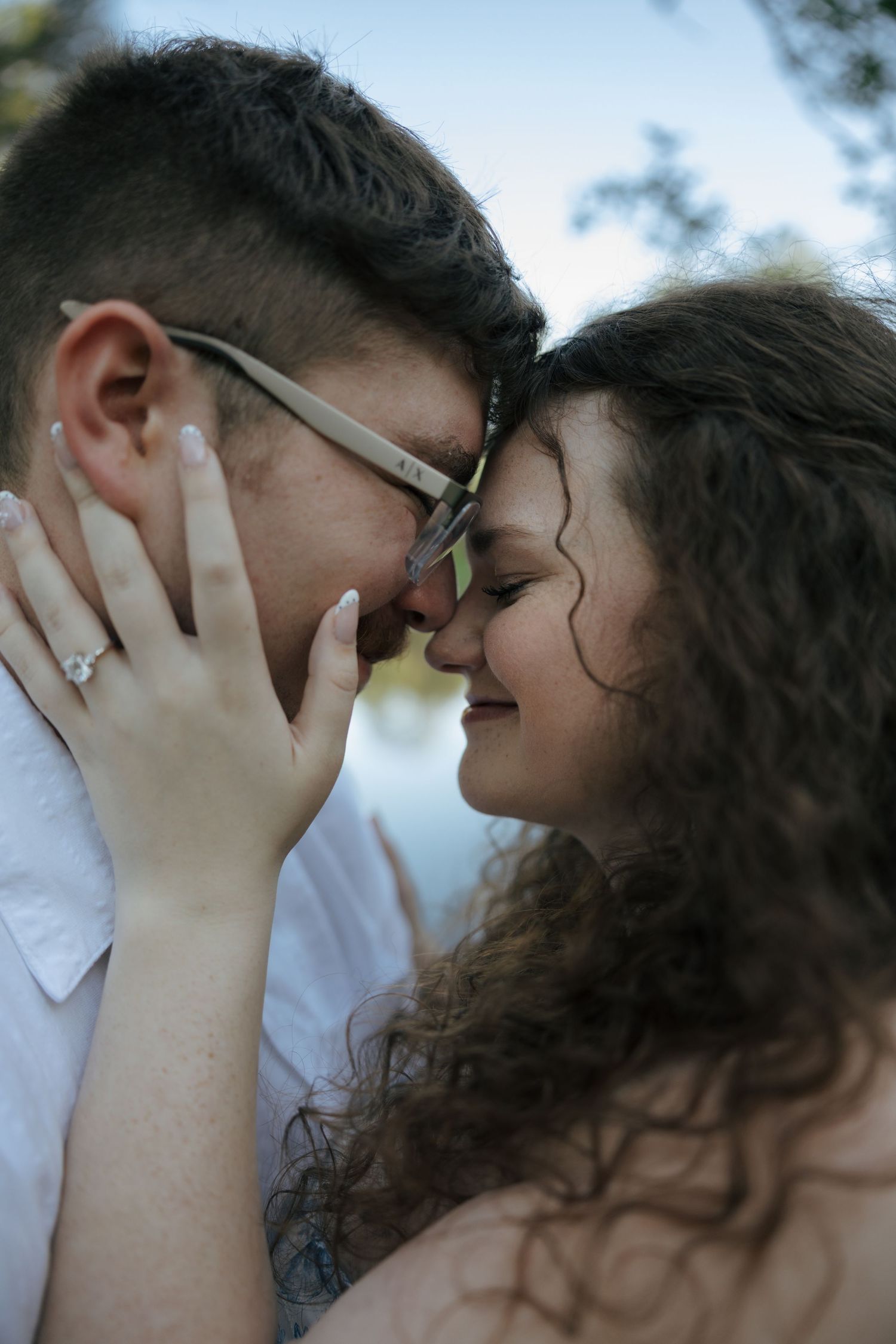 Close-up of an engaged couple touching foreheads, woman displaying diamond ring, sharing a tender romantic moment.