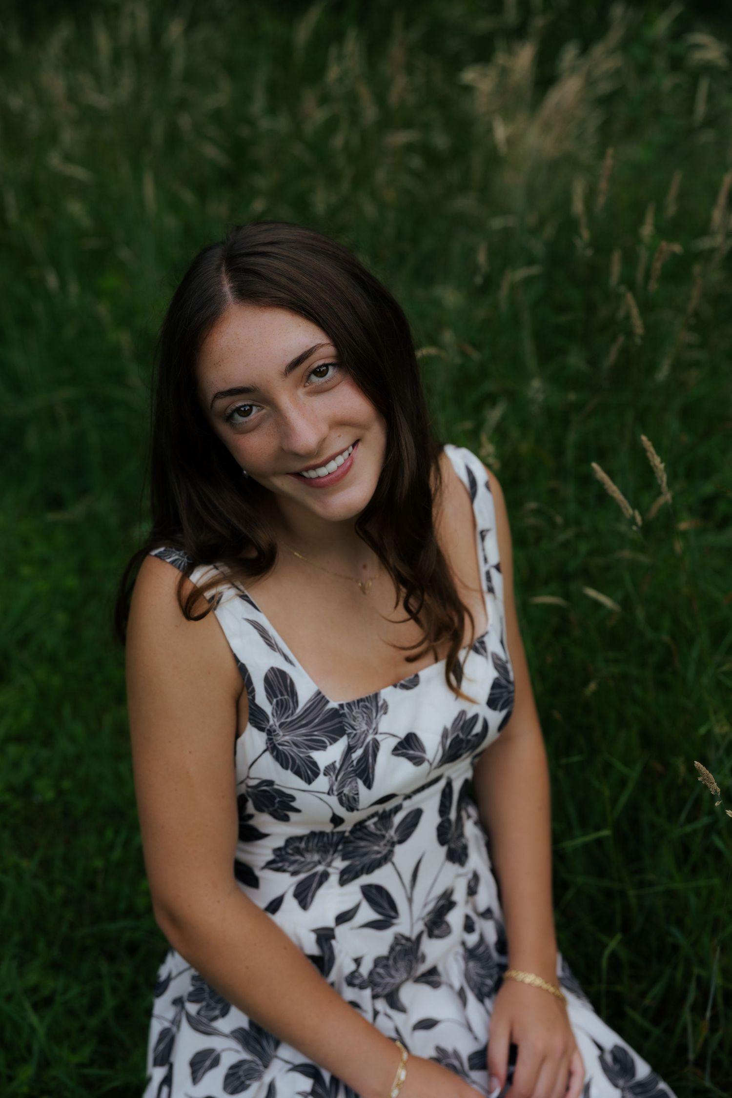 Young woman in floral dress smiling outdoors in green field.