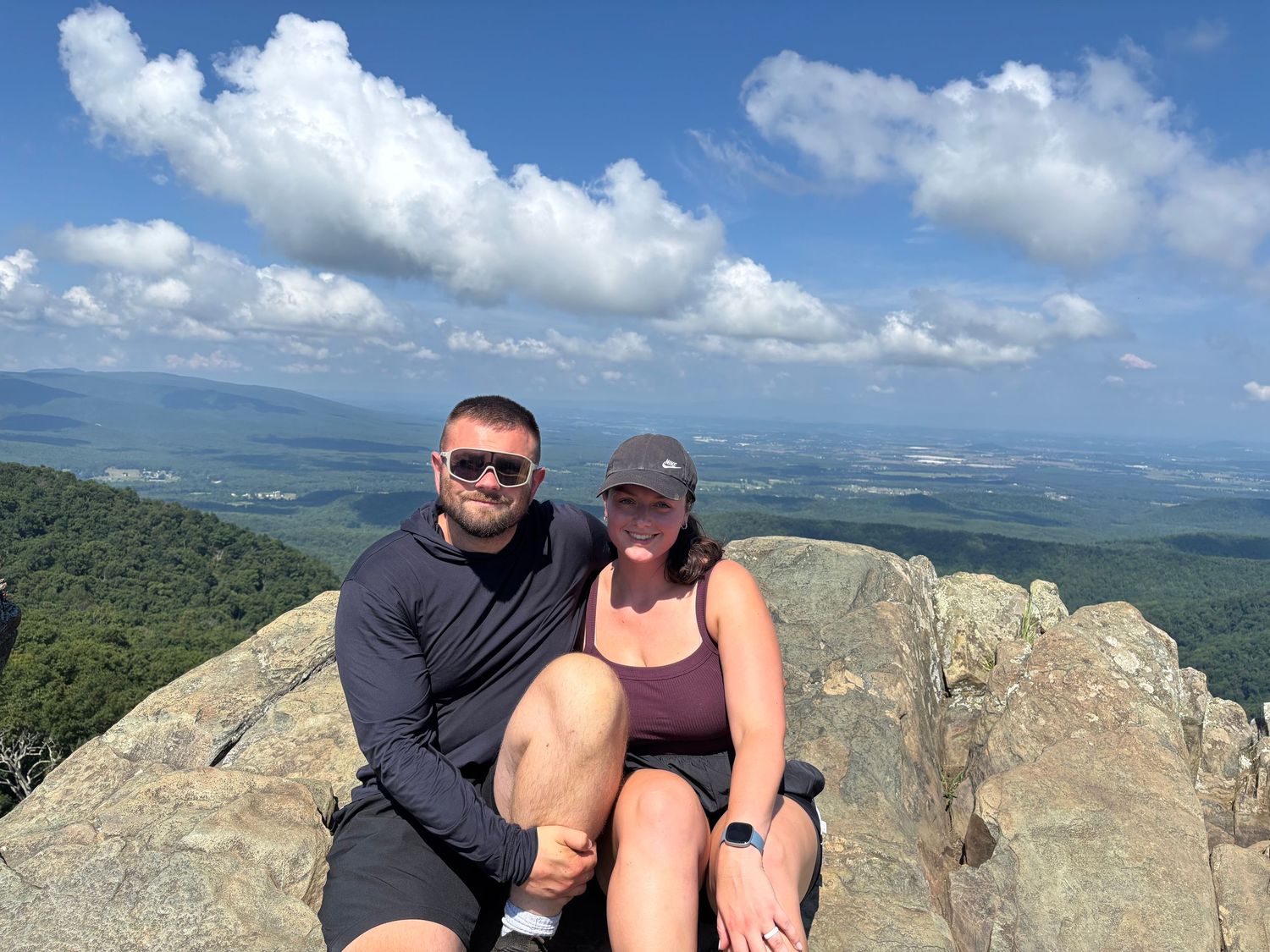 Hikers resting on rocky mountain summit with panoramic valley views in background.
