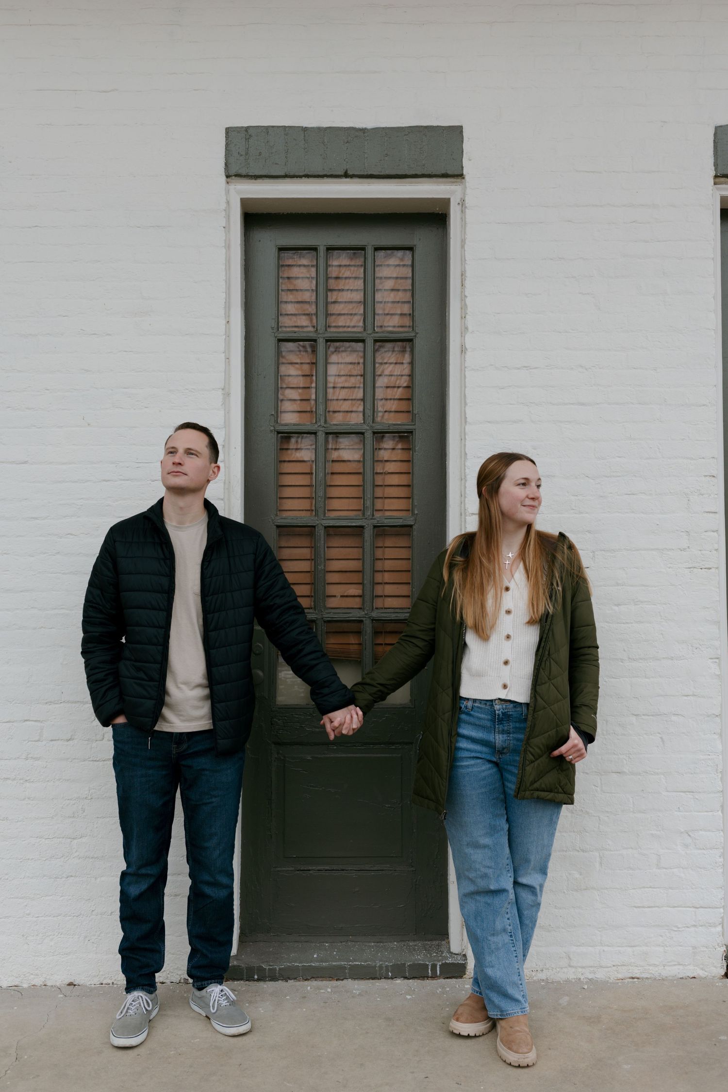 Cropped view of people sitting on a concrete ledge against a white wall with dark green doors.