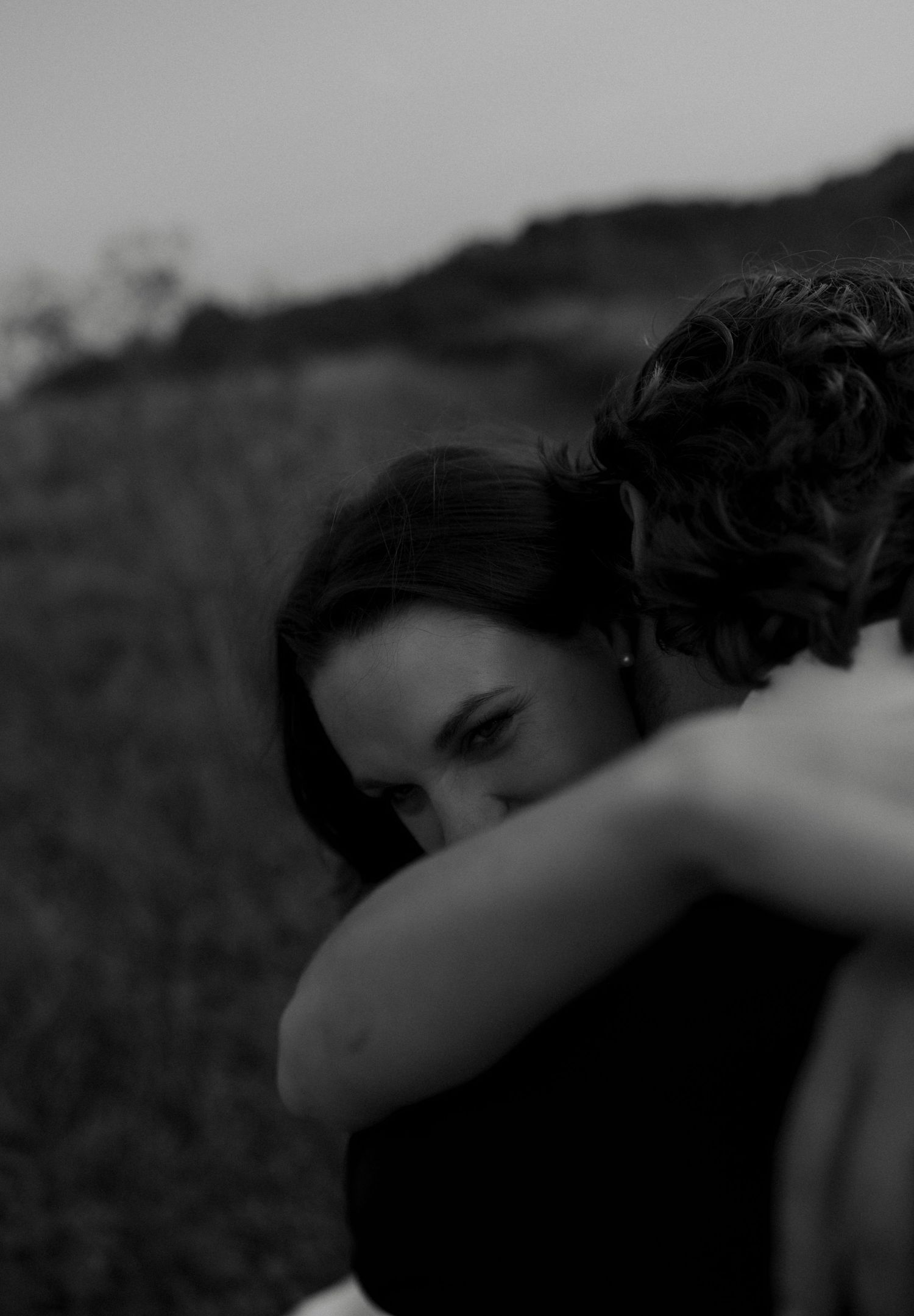 Black and white close-up of bride embracing groom outdoors during golden hour wedding portrait session.