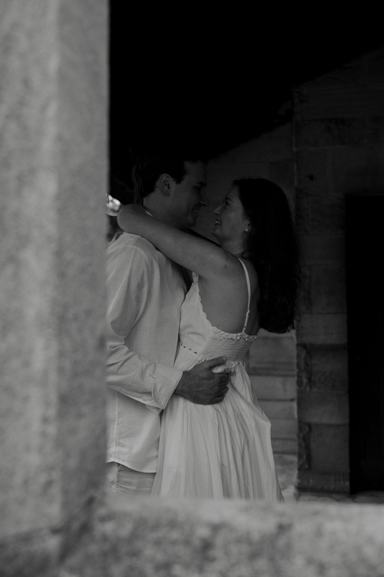 Black and white romantic photo of couple embracing and nearly kissing inside a stone archway.