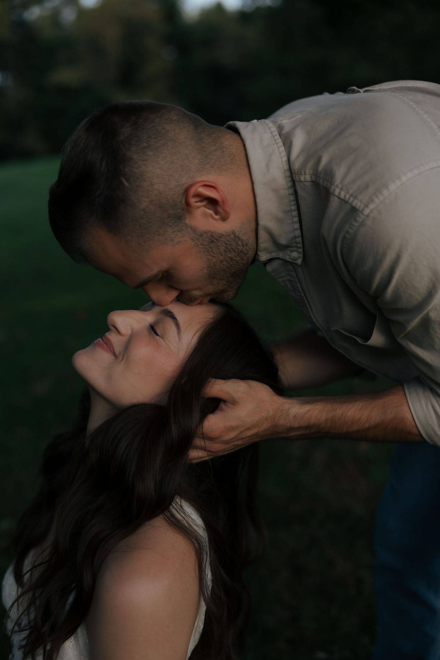 A man tenderly kisses a smiling woman on the forehead outdoors in a romantic couples portrait.