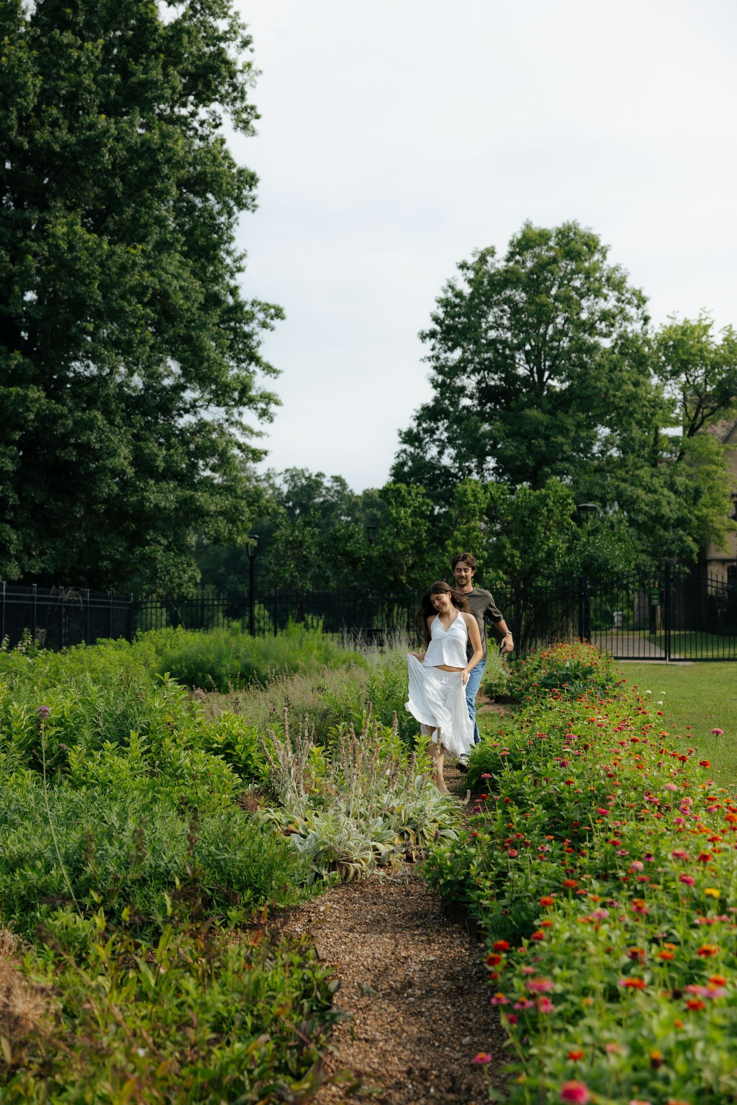A couple walks hand in hand along a garden path lined with colorful flowers and trees.