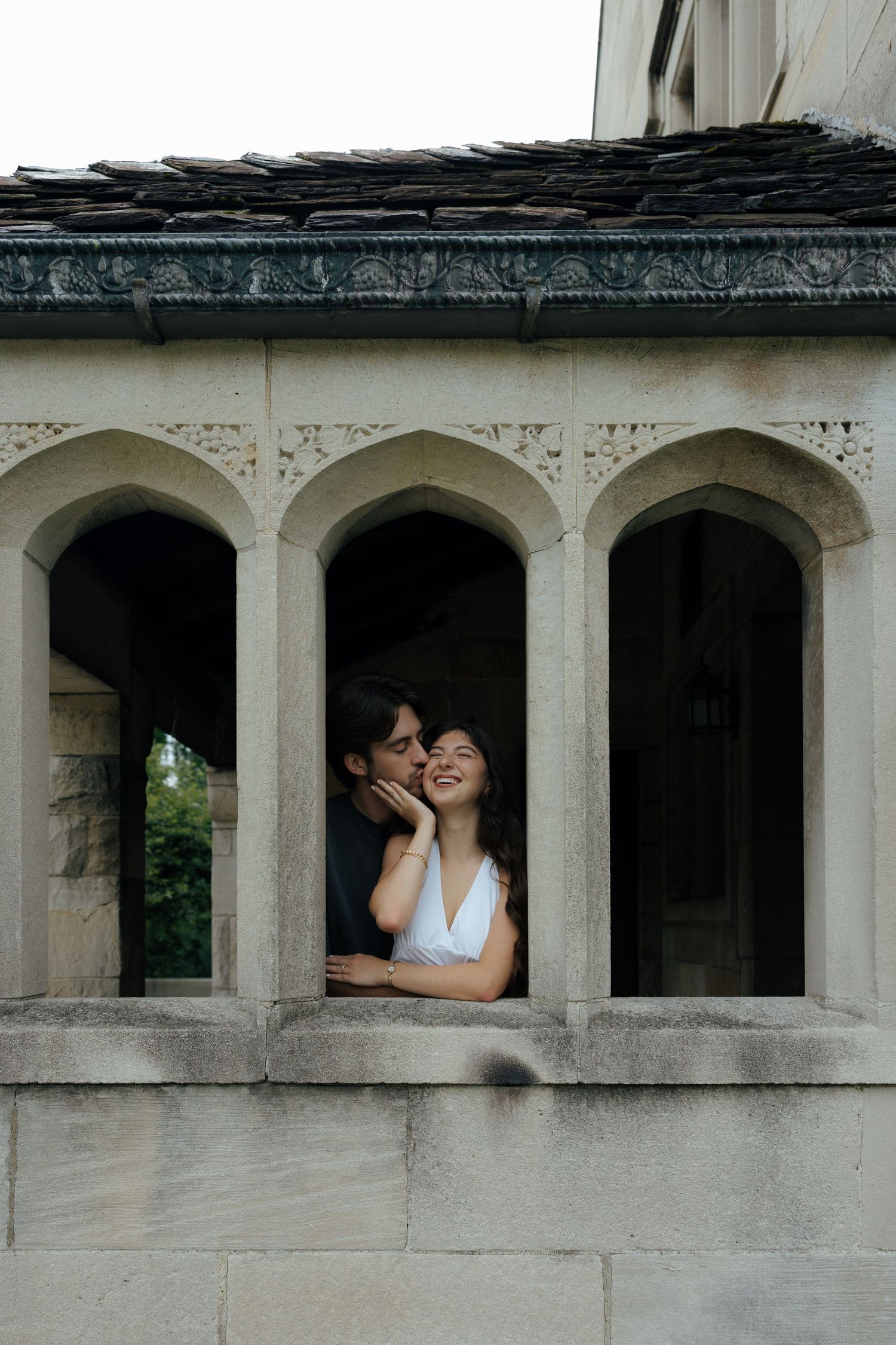 Couple sharing a romantic moment in a stone archway of a historic building, woman smiling joyfully.