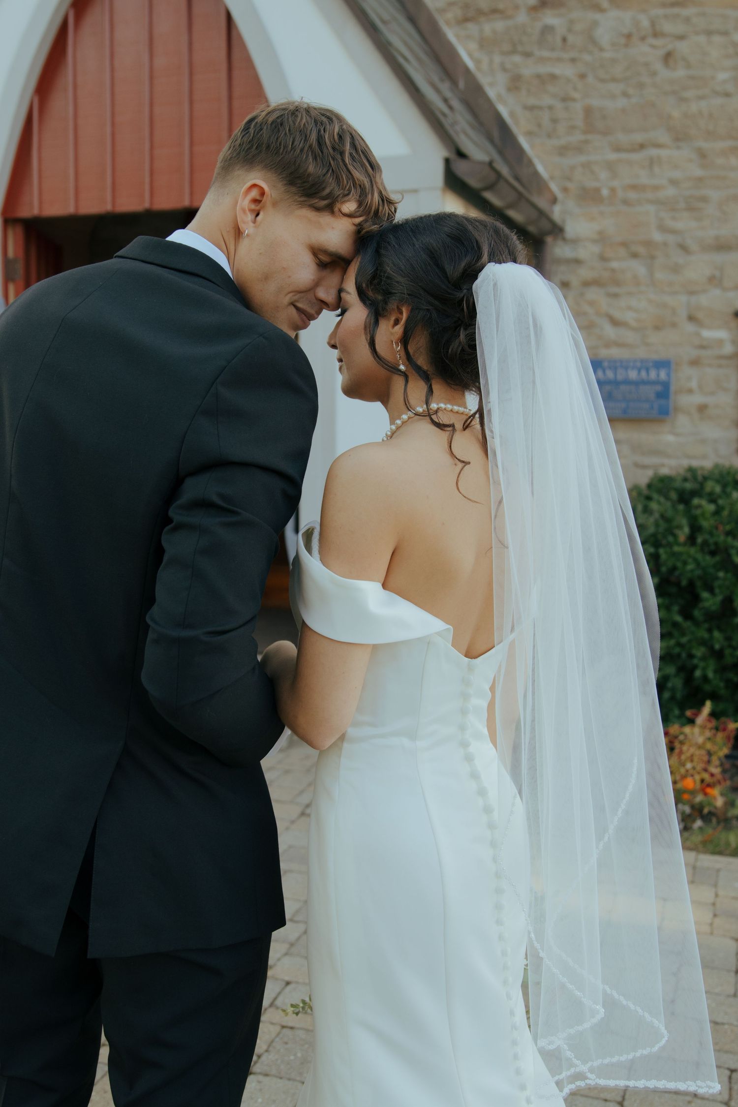 Bride and groom touch foreheads outside stone church.