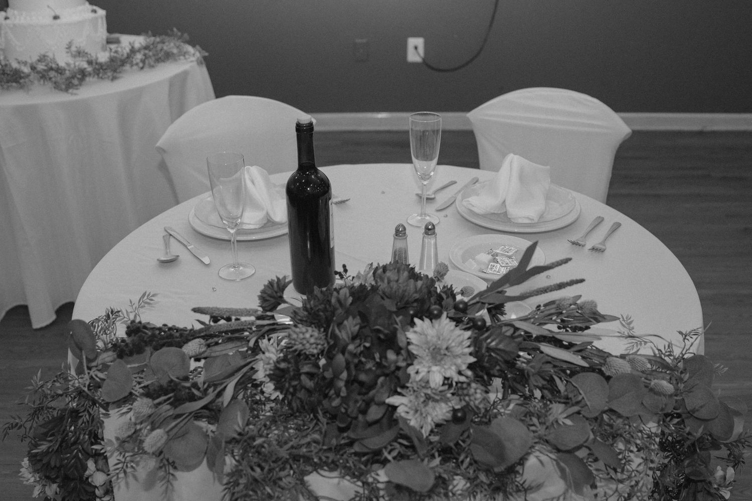 Elegant wedding sweetheart table with floral centerpiece, wine bottle, and place settings.