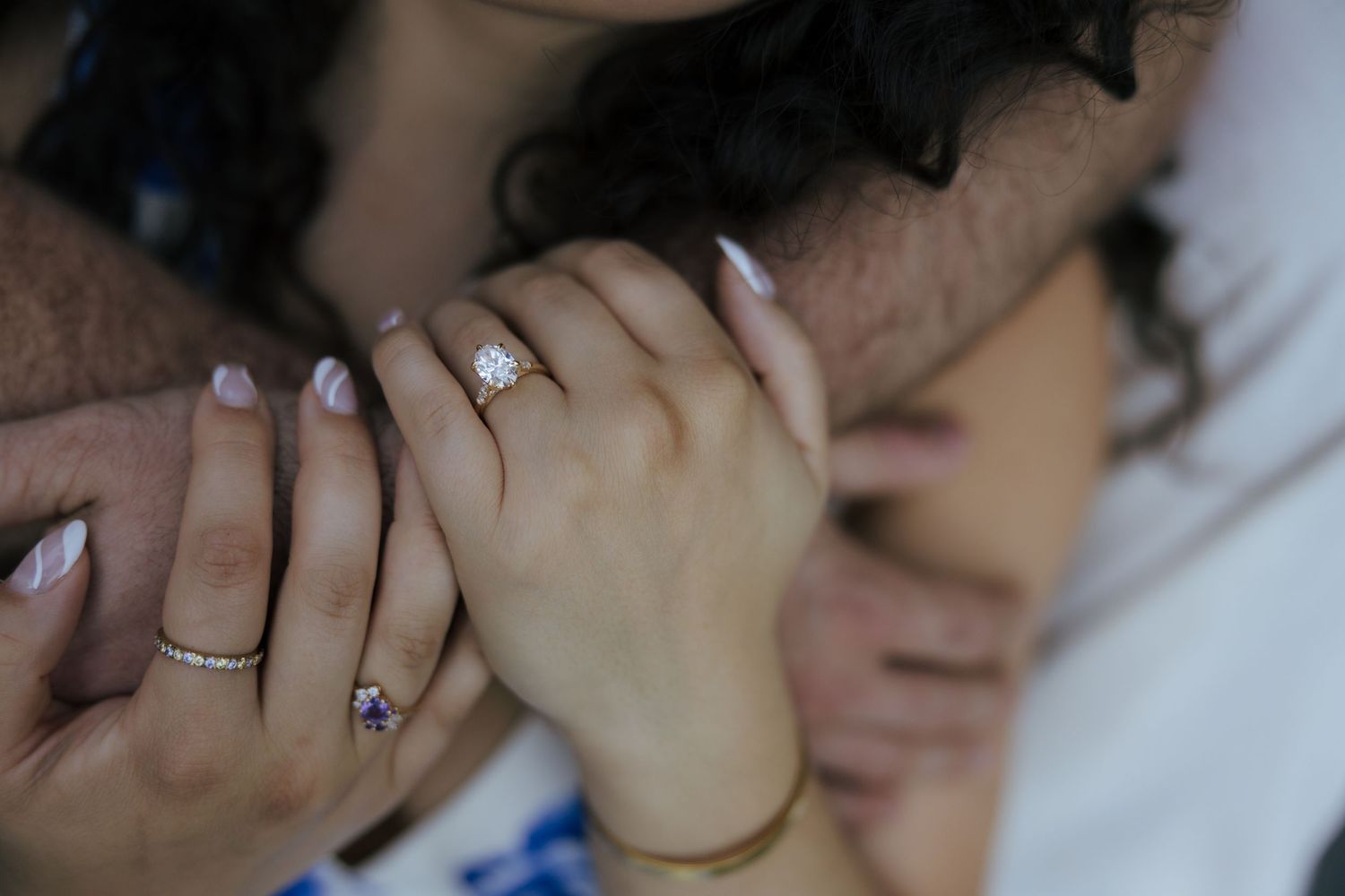 Close-up of an engaged couple holding hands, showcasing a diamond engagement ring with manicured nails.