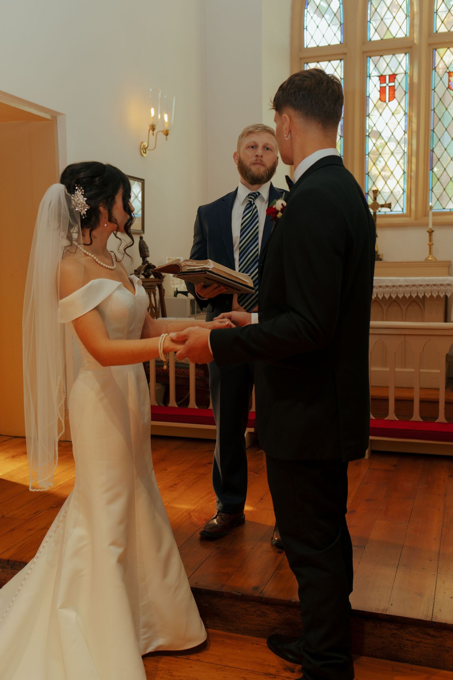 Bride and groom exchange vows holding hands before officiant in a charming church ceremony.