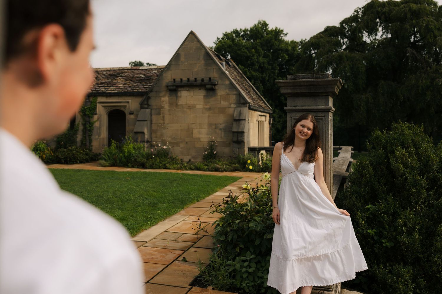 Couple sharing a romantic moment outdoors near a rustic stone building with lush gardens.