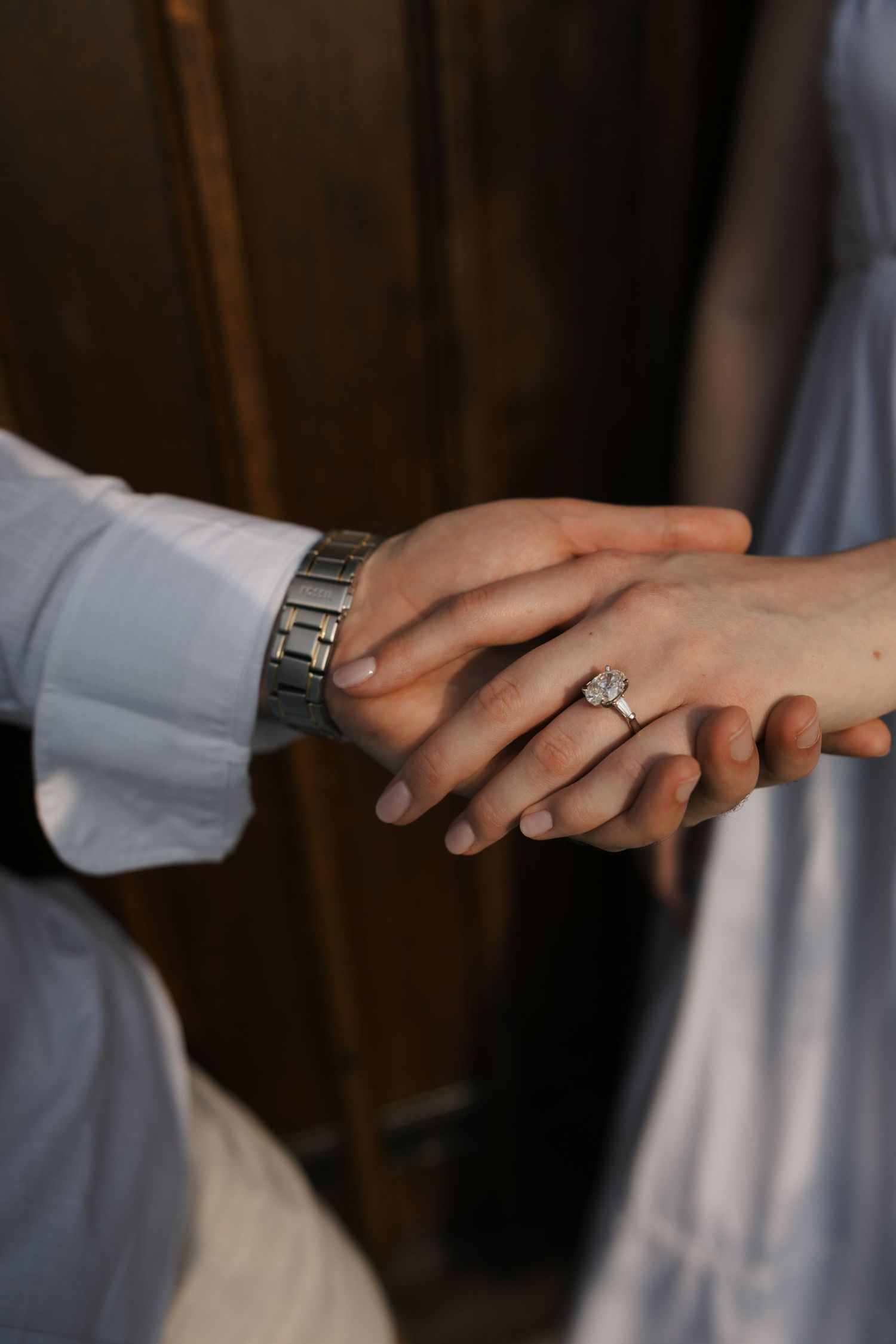 Close-up of couple holding hands showing engagement ring and silver watch during romantic proposal moment.