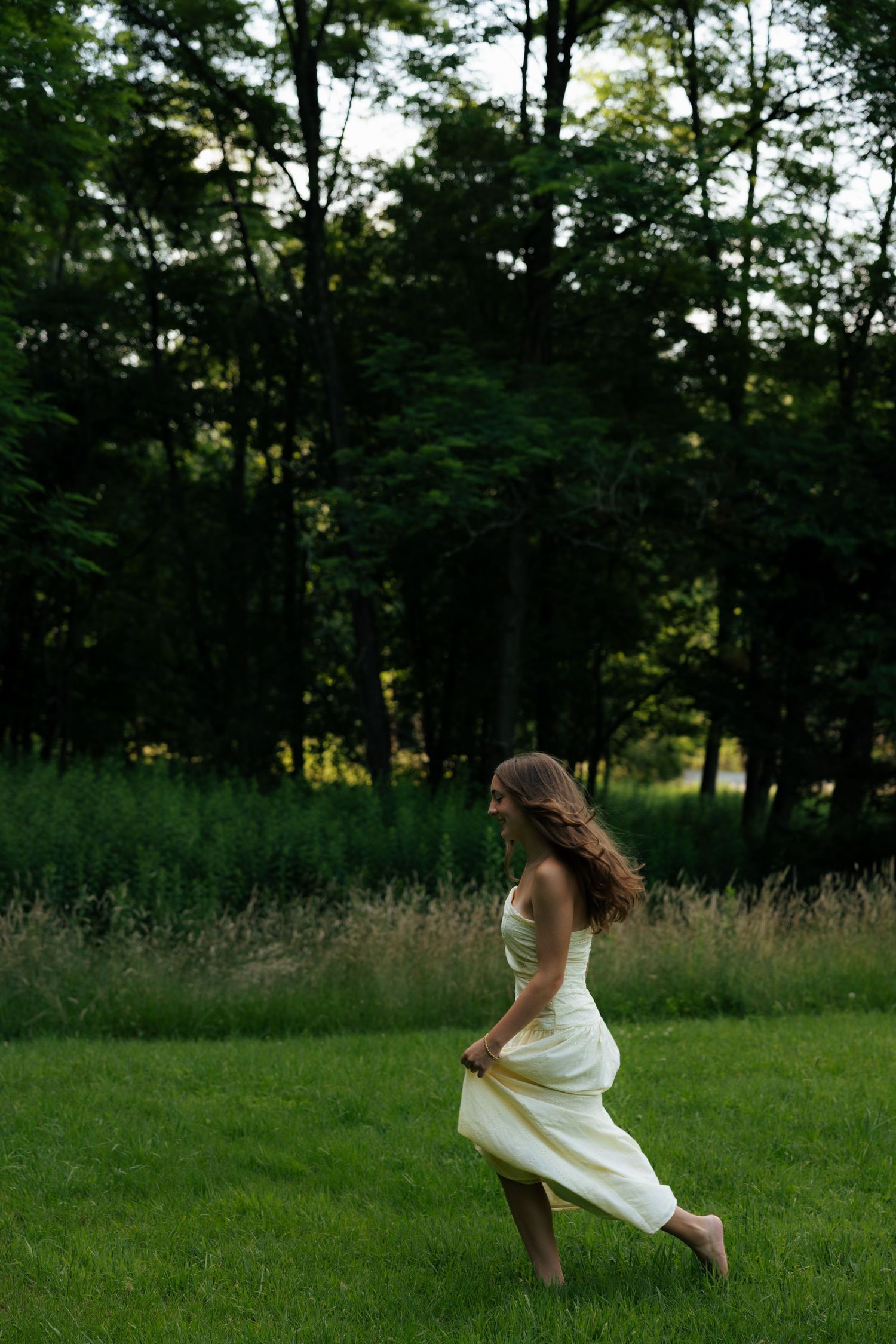 Woman in white dress walking barefoot on lush green grass with trees in background.