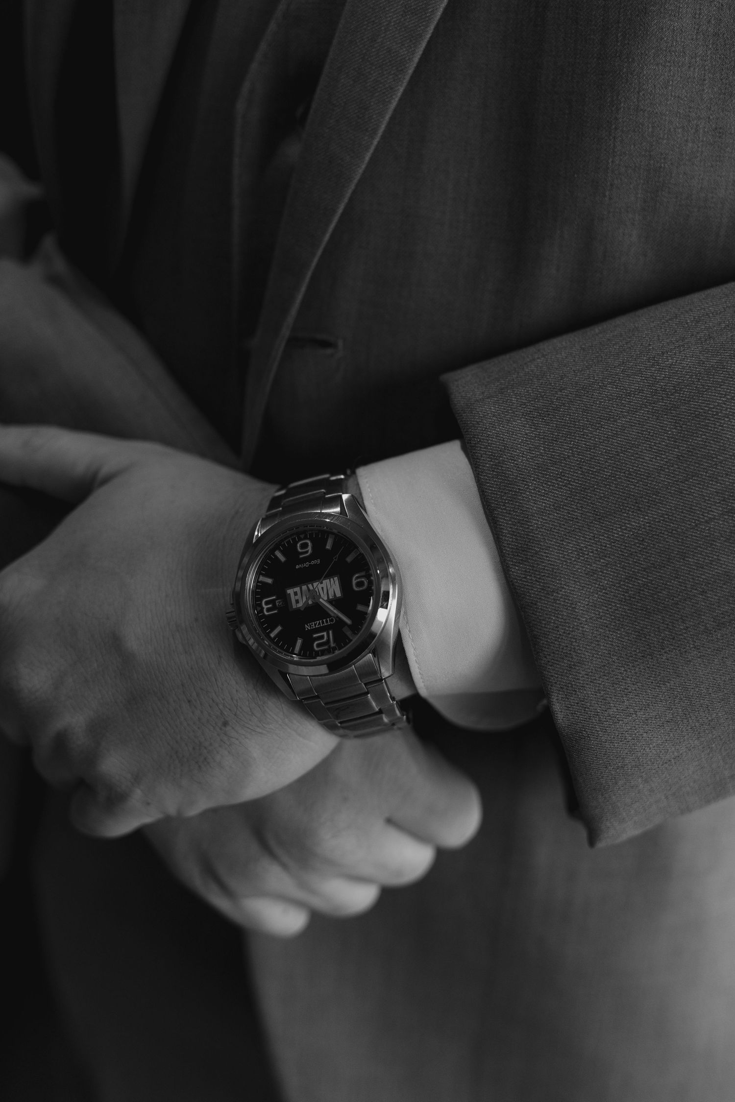 Black and white close-up of a man in a suit adjusting a silver analog-digital watch on his wrist.