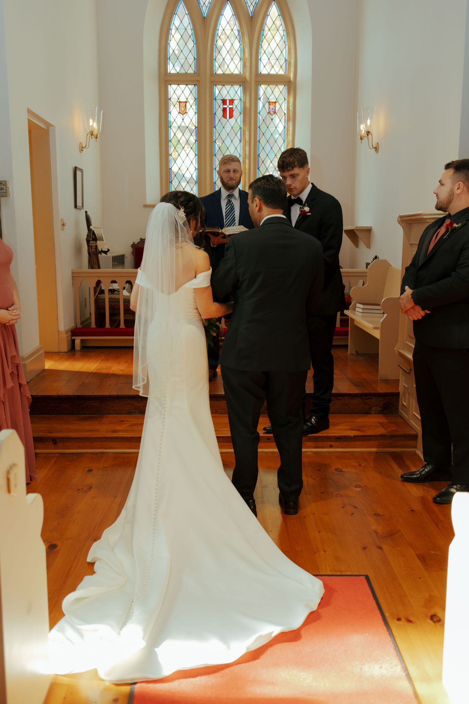 Bride and groom exchange vows at the altar of a charming white church with stained glass windows.