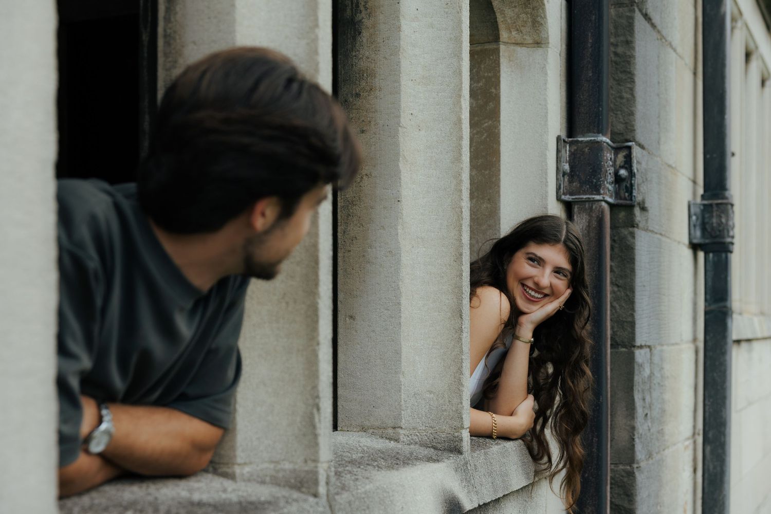 A smiling woman leans on a stone ledge while a man looks at her between historic columns.