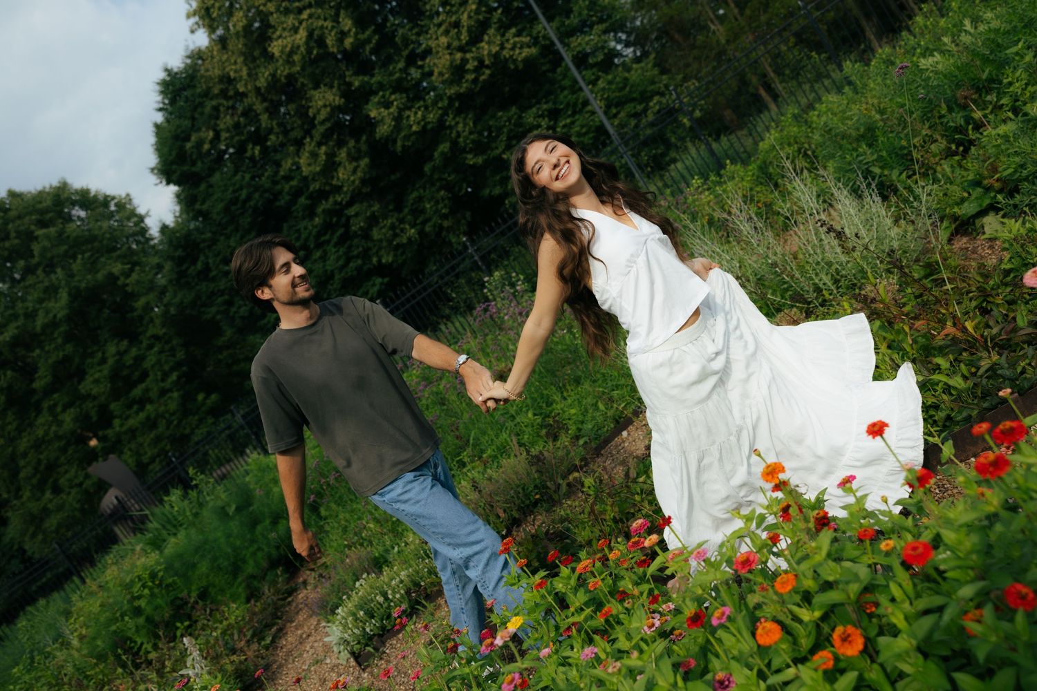 Joyful couple holding hands walking through a colorful flower garden on a cloudy day.