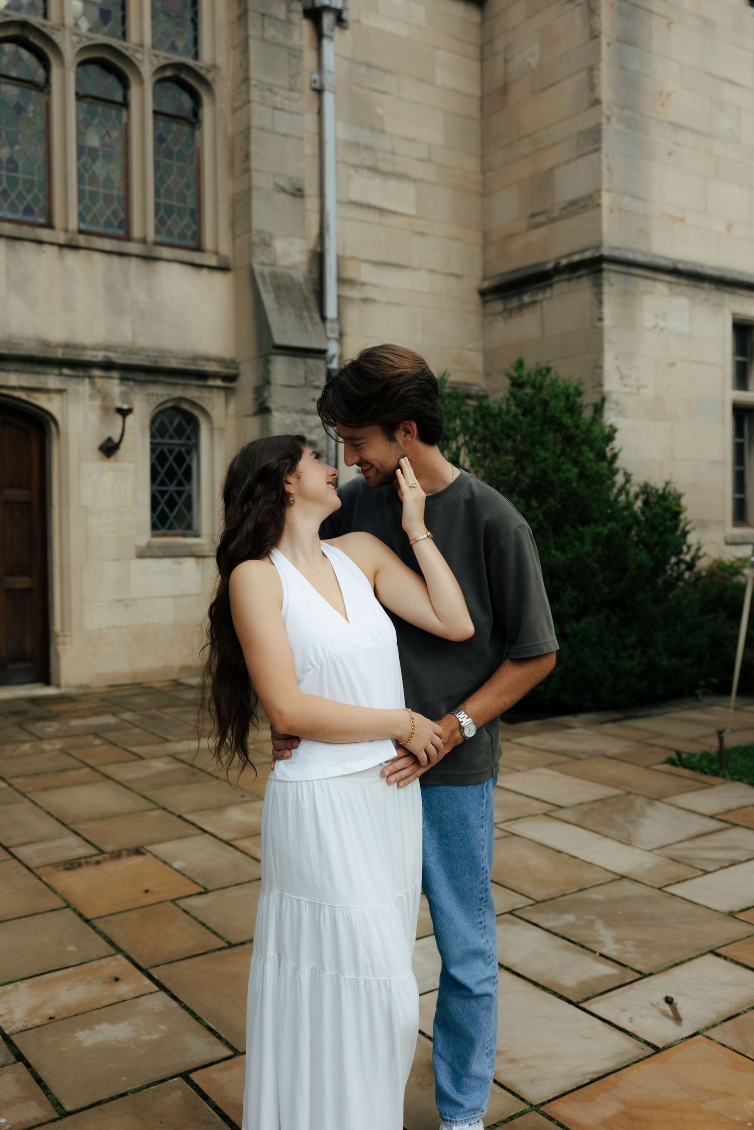 Engaged couple sharing a tender moment gazing at each other outside historic gothic stone building.