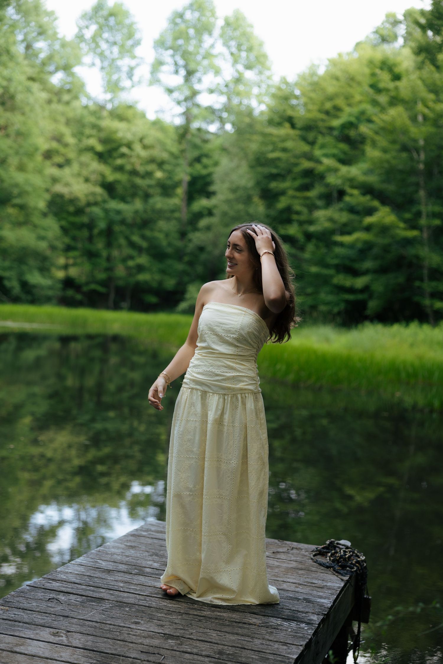 Woman in yellow strapless gown standing on wooden dock by lake.