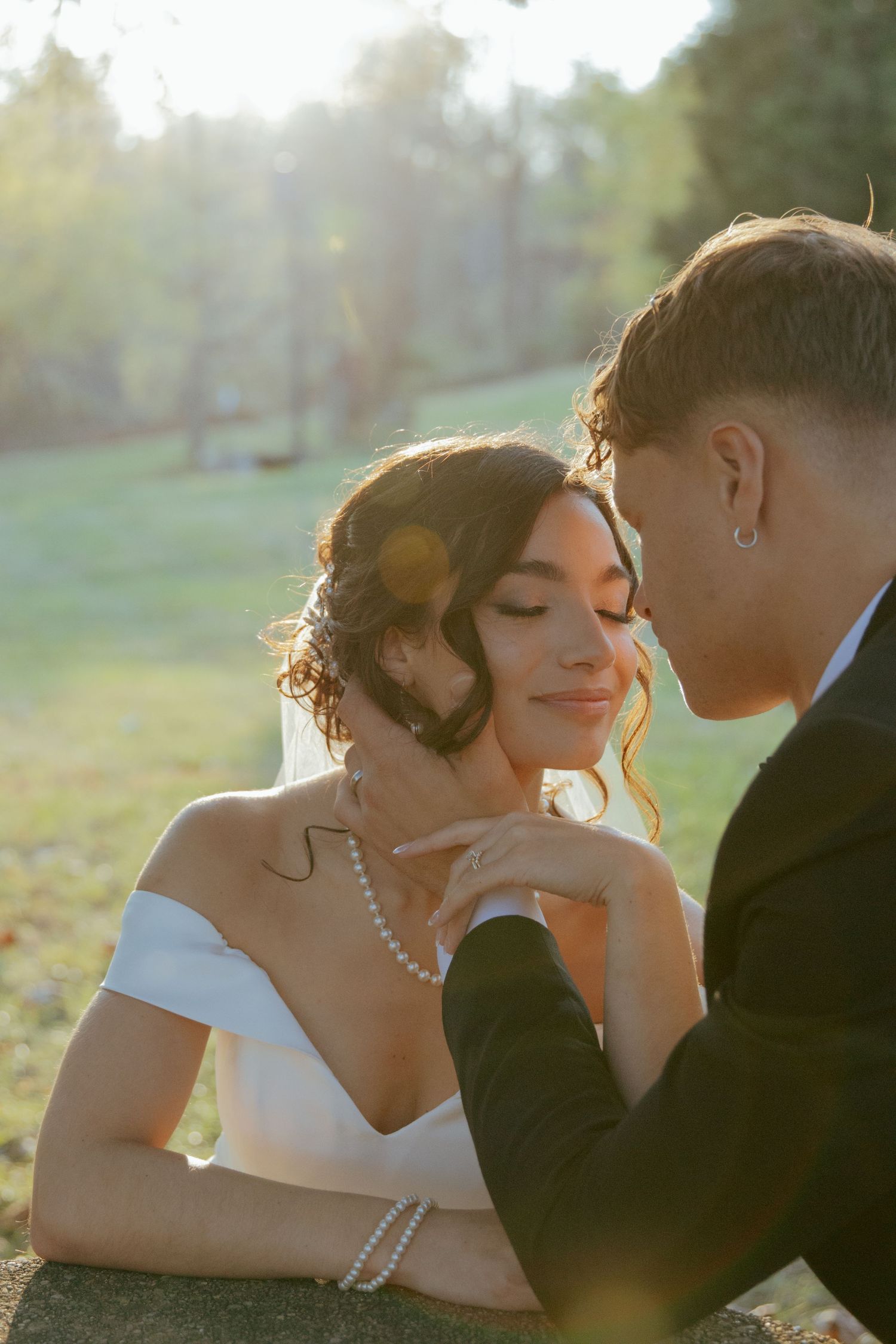 Bride and groom share tender moment in golden sunlight outdoors on their wedding day.