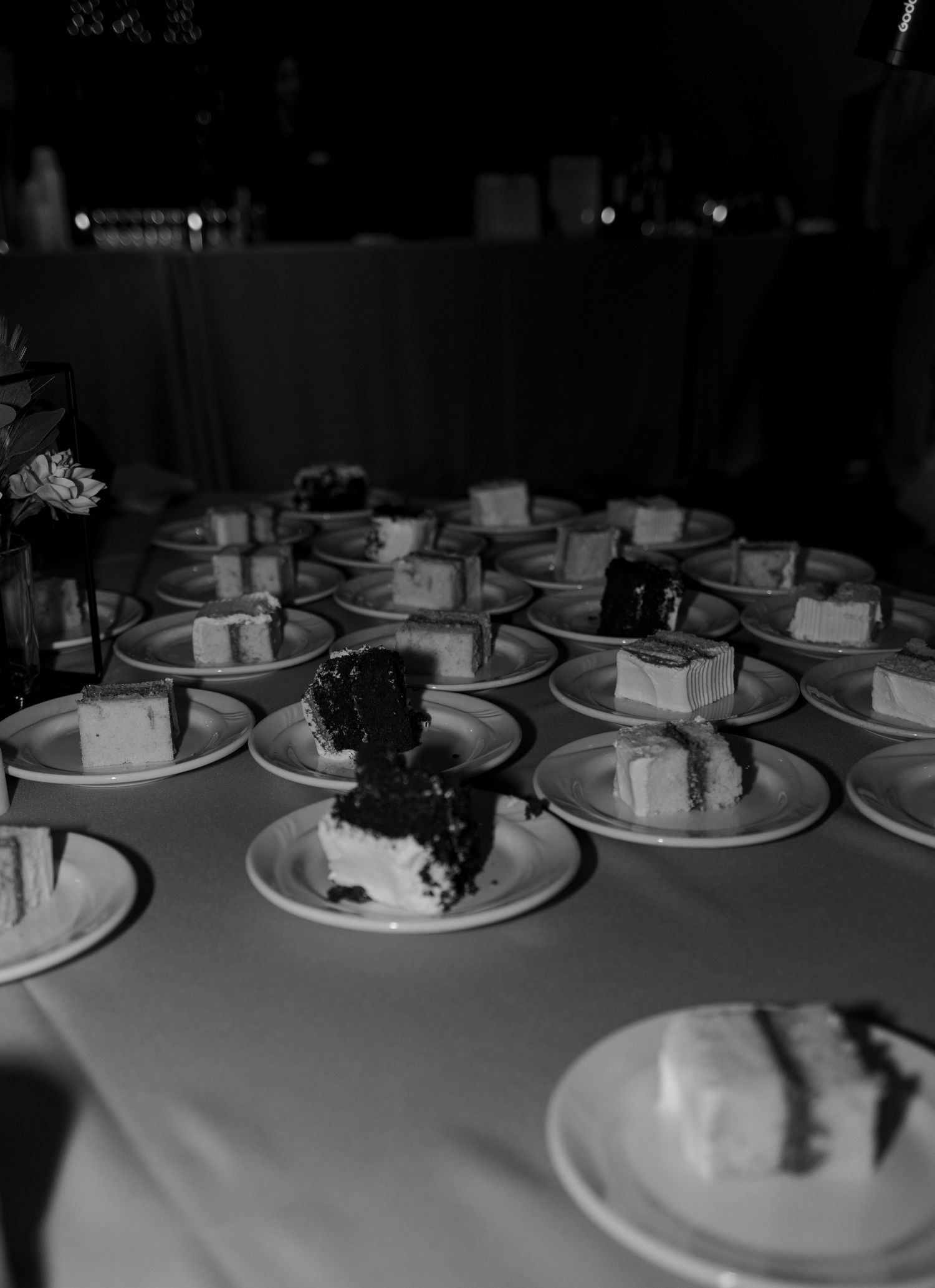 Multiple slices of wedding cake served on white plates arranged on a banquet table in black and white photo.