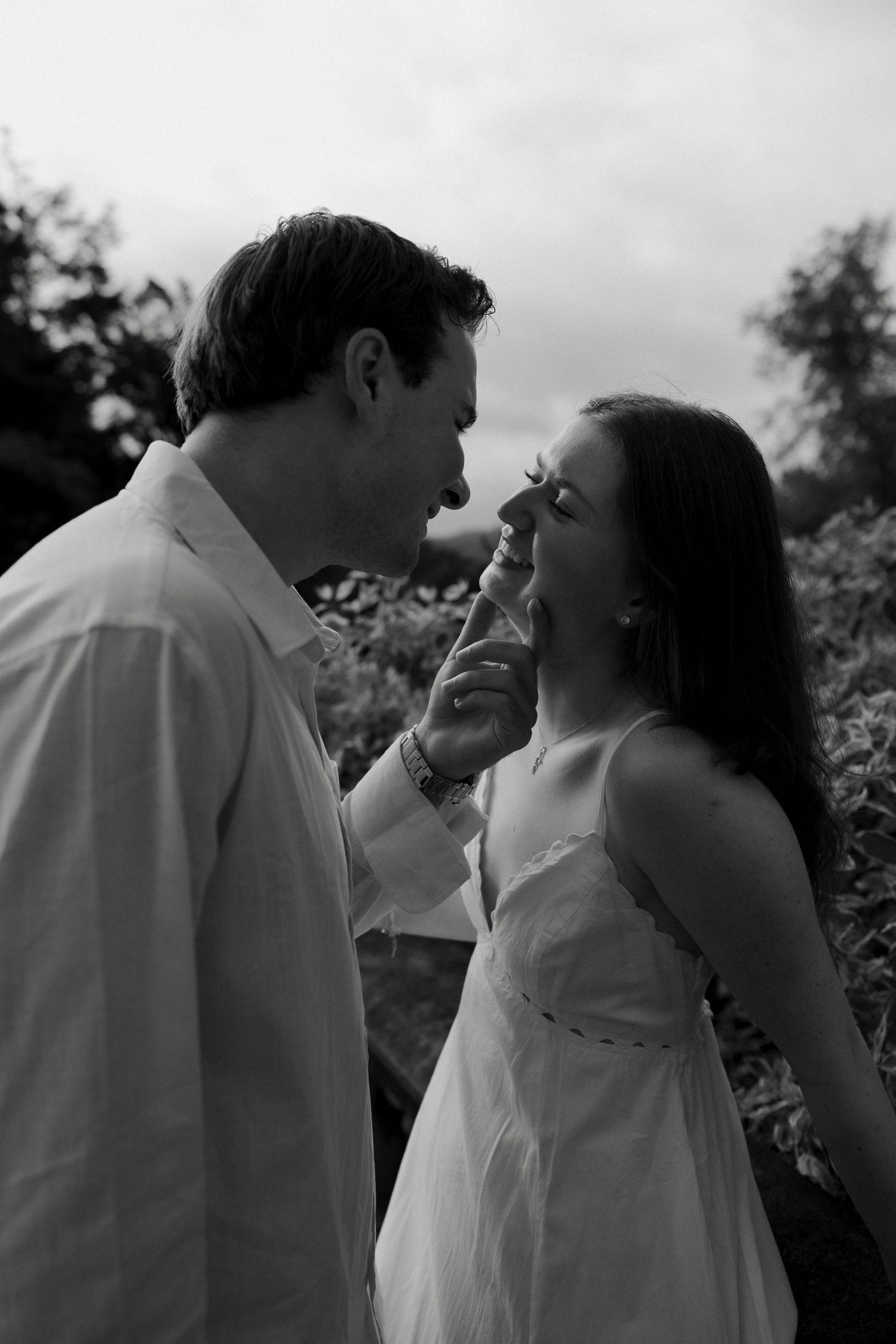 Black and white romantic portrait of a couple almost kissing outdoors, man gently touching womans face.