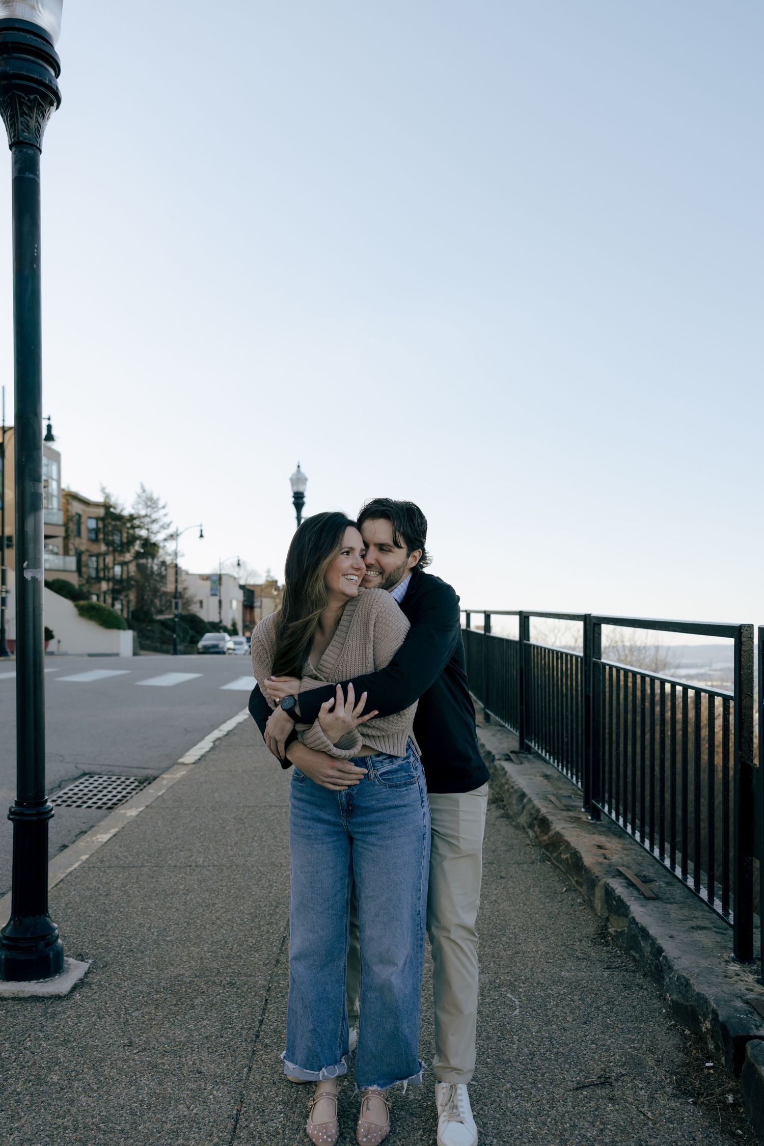 A couple shares a romantic moment while walking along a waterfront promenade at dusk.