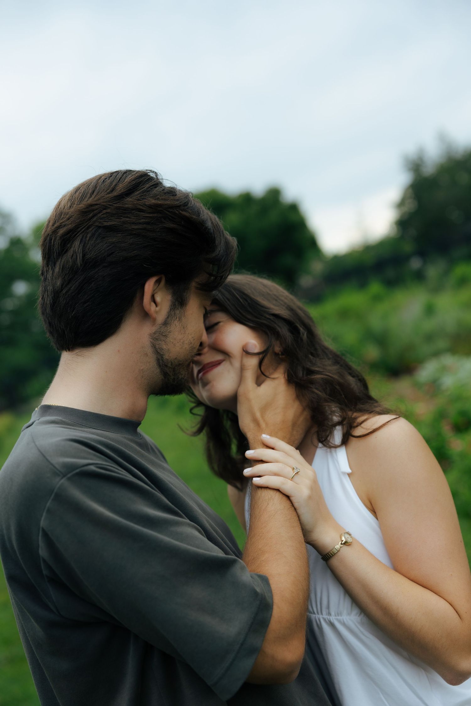 Couple sharing a tender moment outdoors, almost kissing in a lush green garden setting.