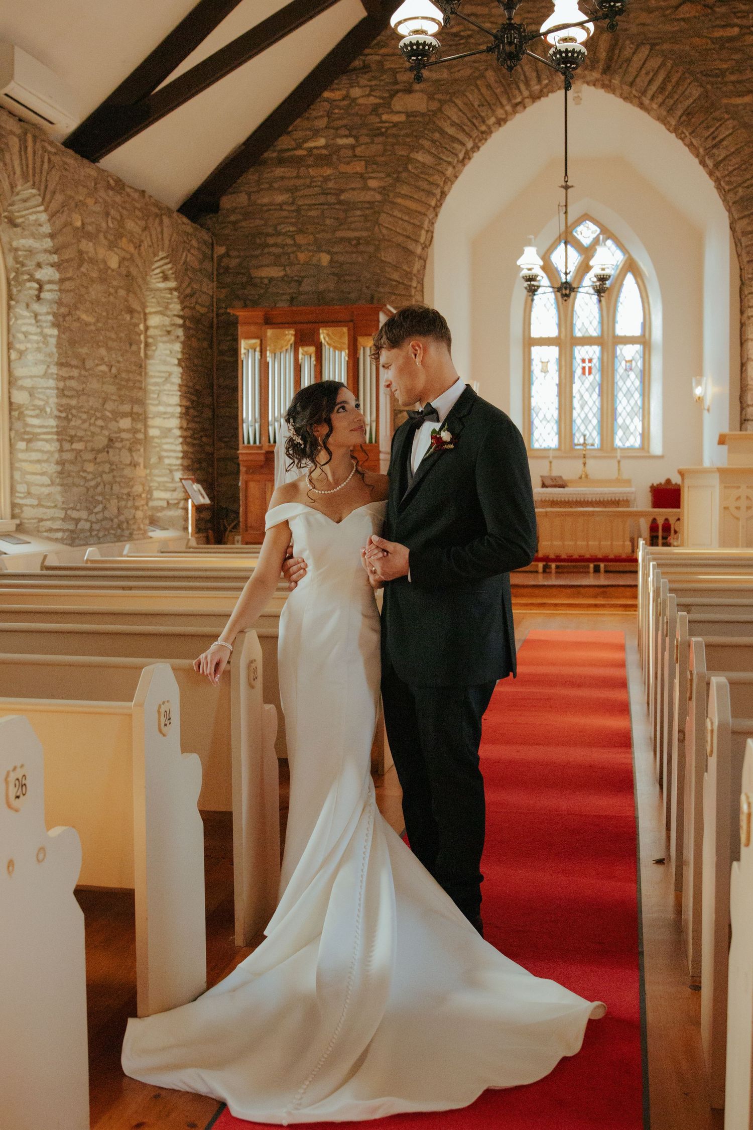 Bride and groom share an intimate moment in the aisle of a beautiful stone church with red carpet.