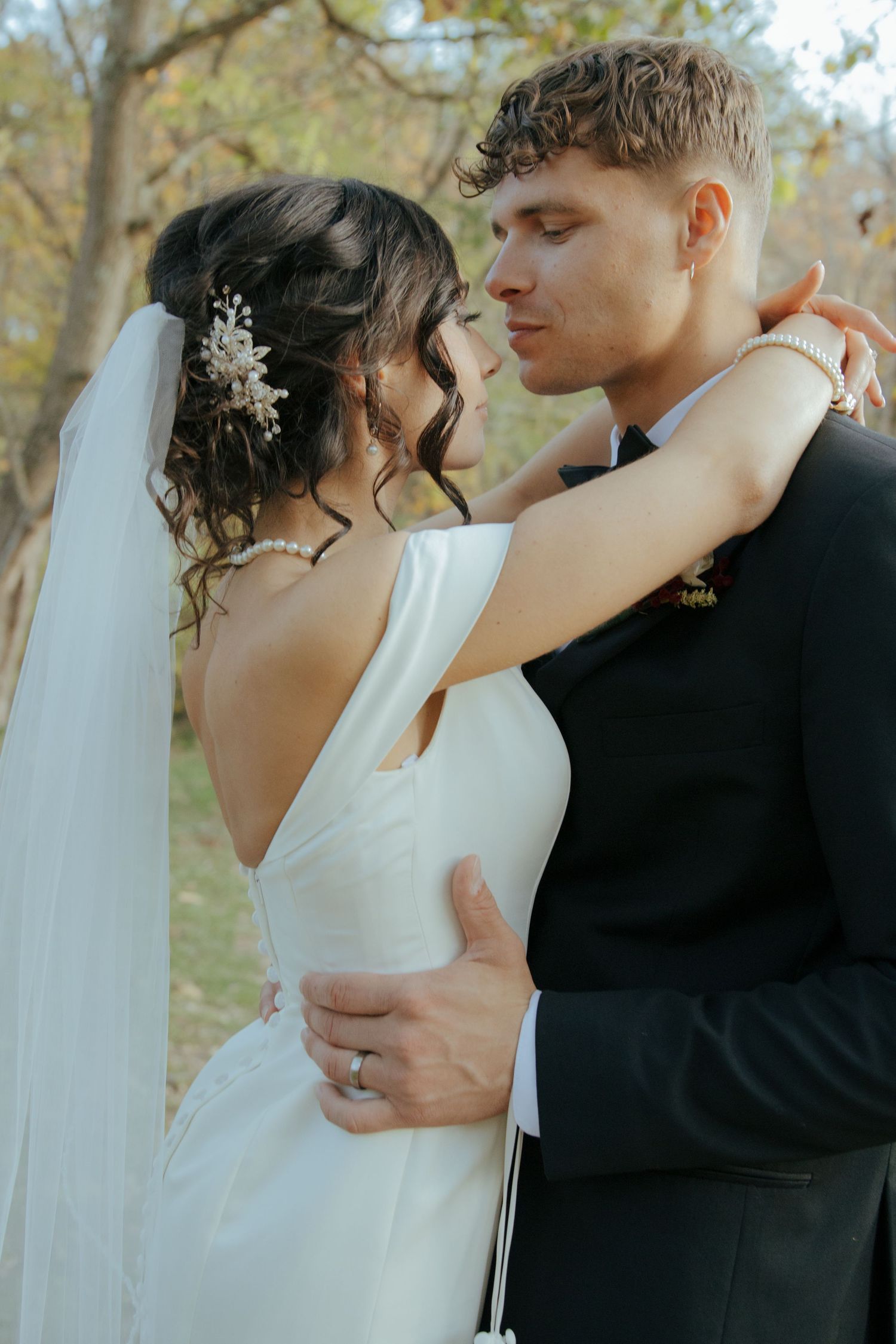Bride and groom share a romantic embrace outdoors surrounded by autumn foliage on their wedding day.