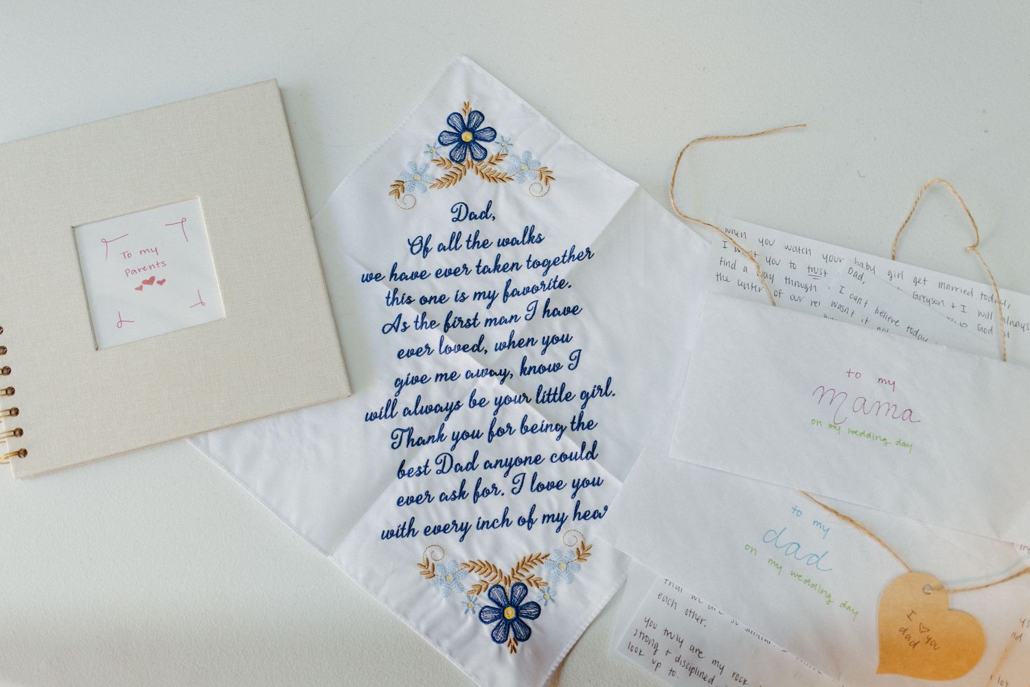 Embroidered wedding handkerchief with heartfelt message to Dad displayed alongside a guest book and wedding stationery.