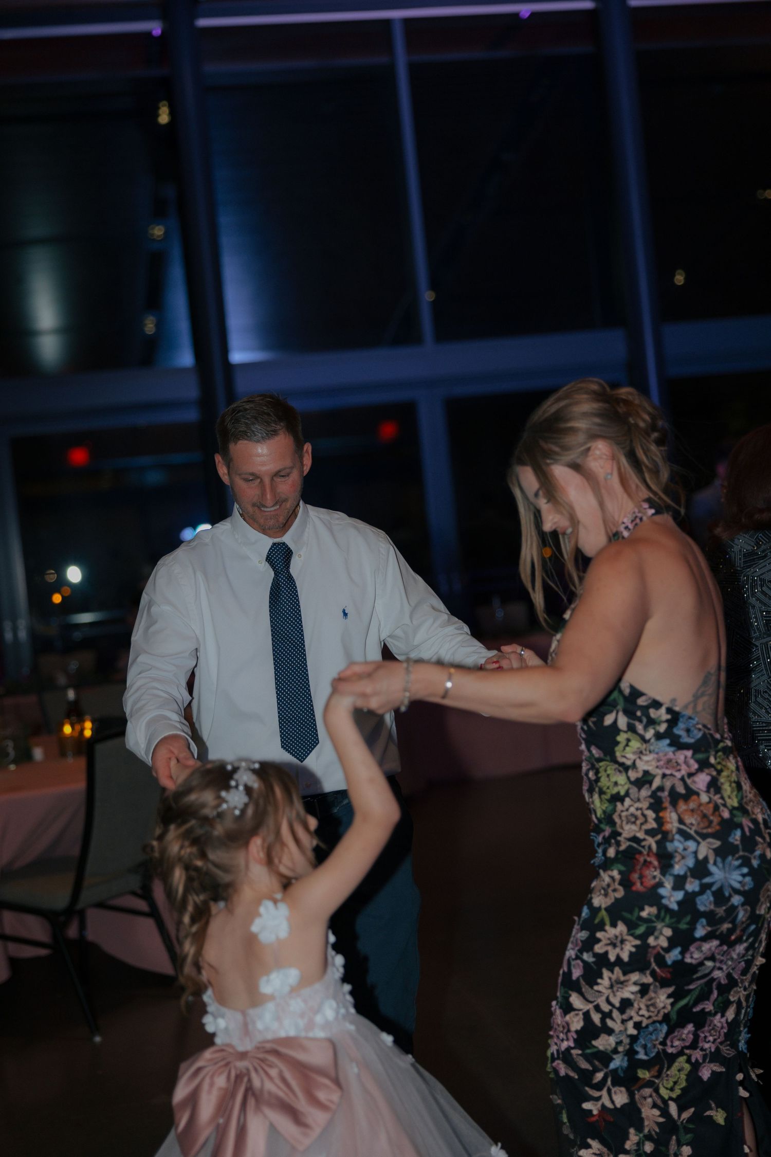 Man and woman dance with young flower girl in pink dress at wedding reception on dance floor.