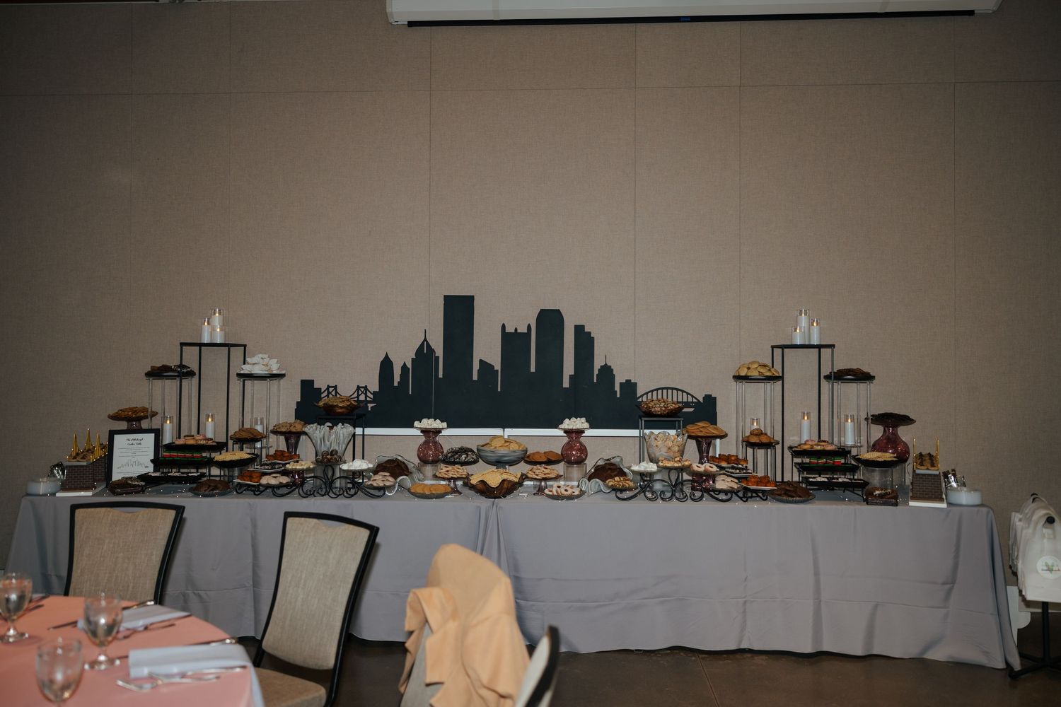 Elegant dessert table with city skyline backdrop, displaying assorted treats on tiered stands at a banquet event.