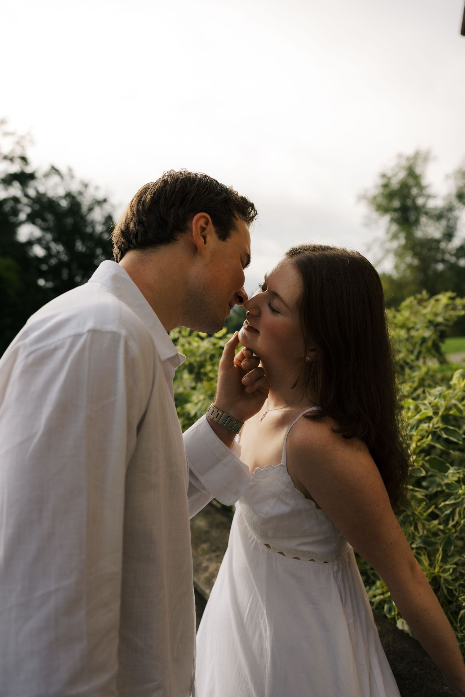 A couple shares a romantic almost-kiss outdoors, the man gently cupping the woman's face in soft light.