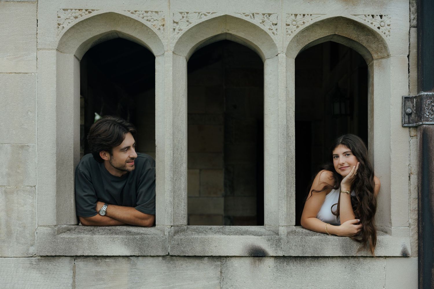 A couple leans out of separate arched stone windows, sharing a quiet moment on a historic building.
