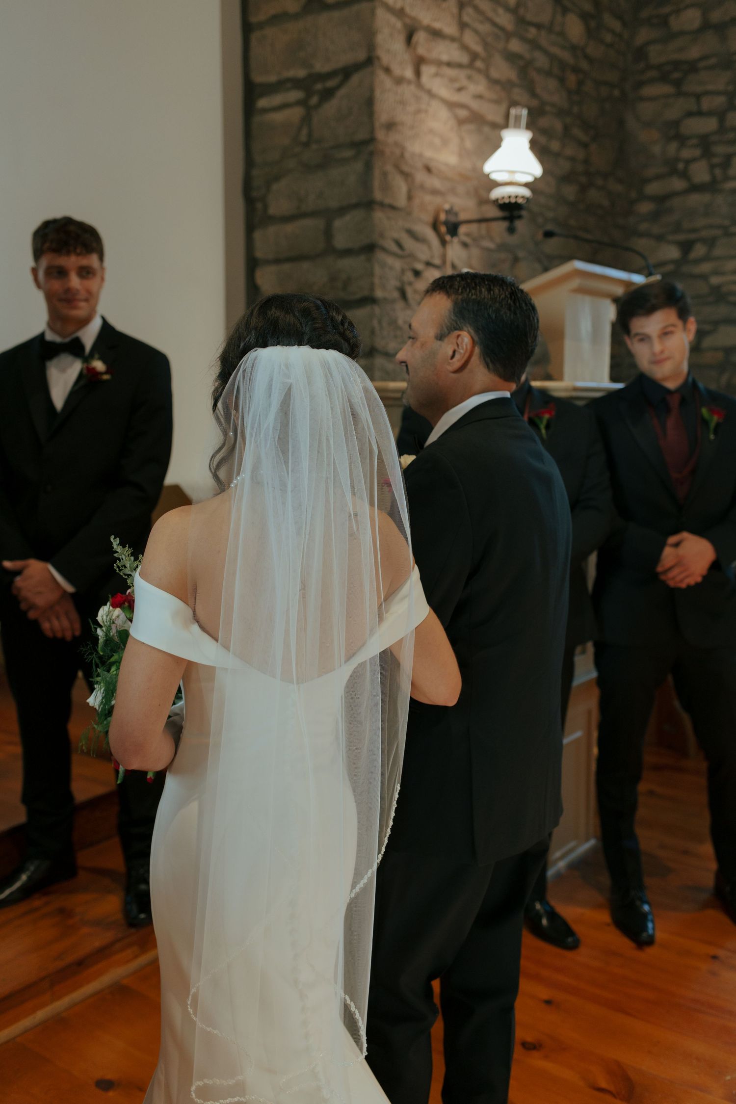 Bride in white gown and veil exchanges vows at stone church altar with groom.