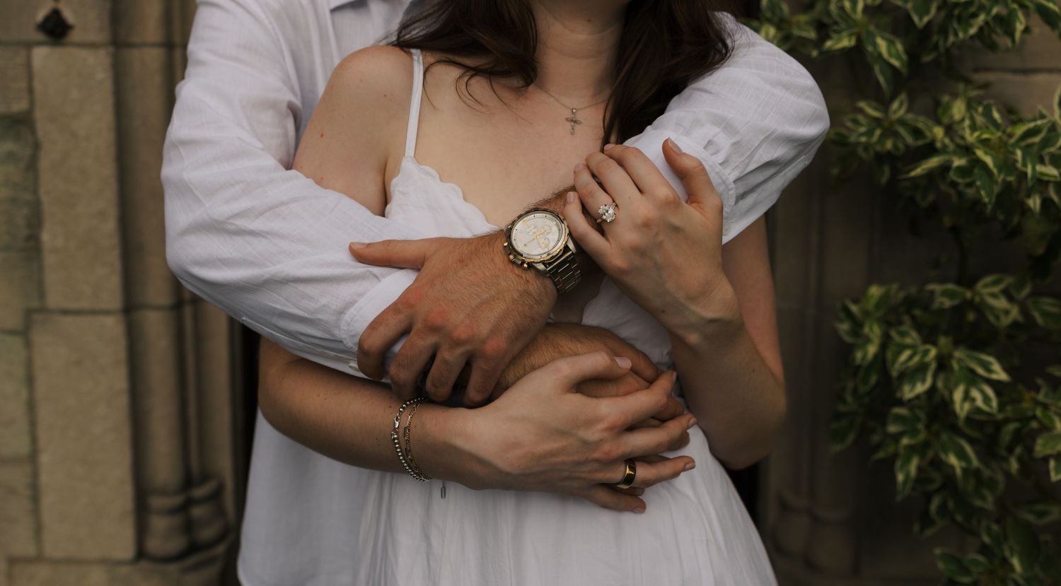 Close-up of couple embracing, woman in white dress with gold watch and bracelet accessories.