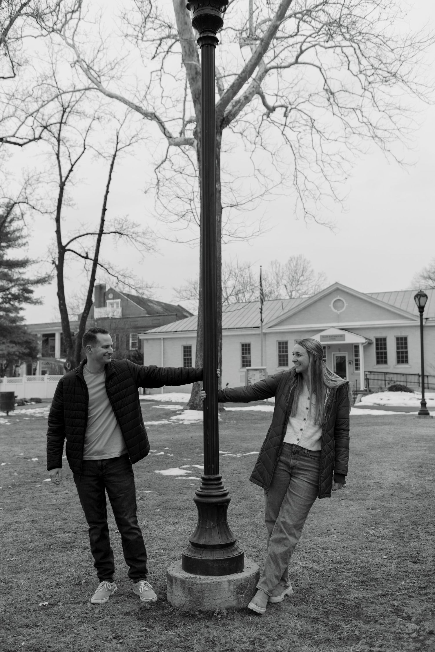 Two figures playfully pose and interact around a vintage-style lamp post in a series of black and white photographs.
