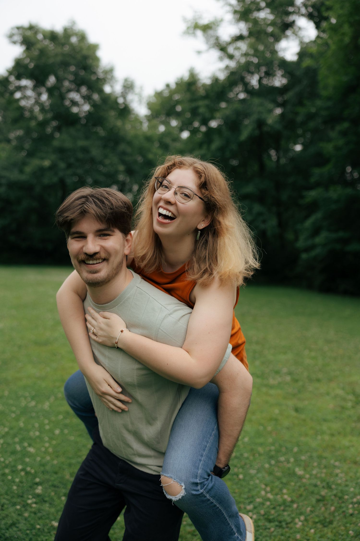 Man gives laughing woman piggyback ride on green grass in park.