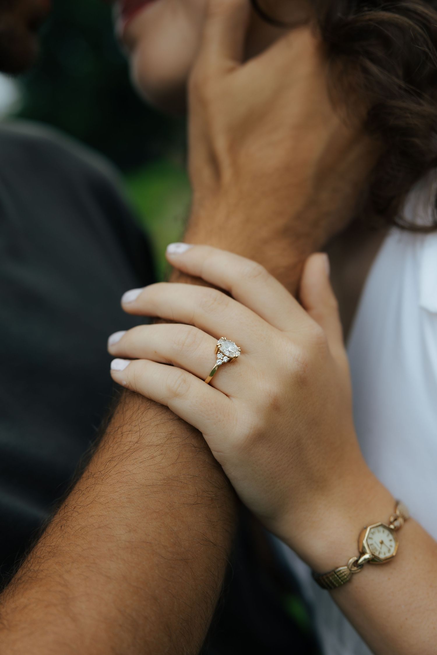 Close-up of woman's hand showing a gold engagement ring with a watch bracelet on her wrist.