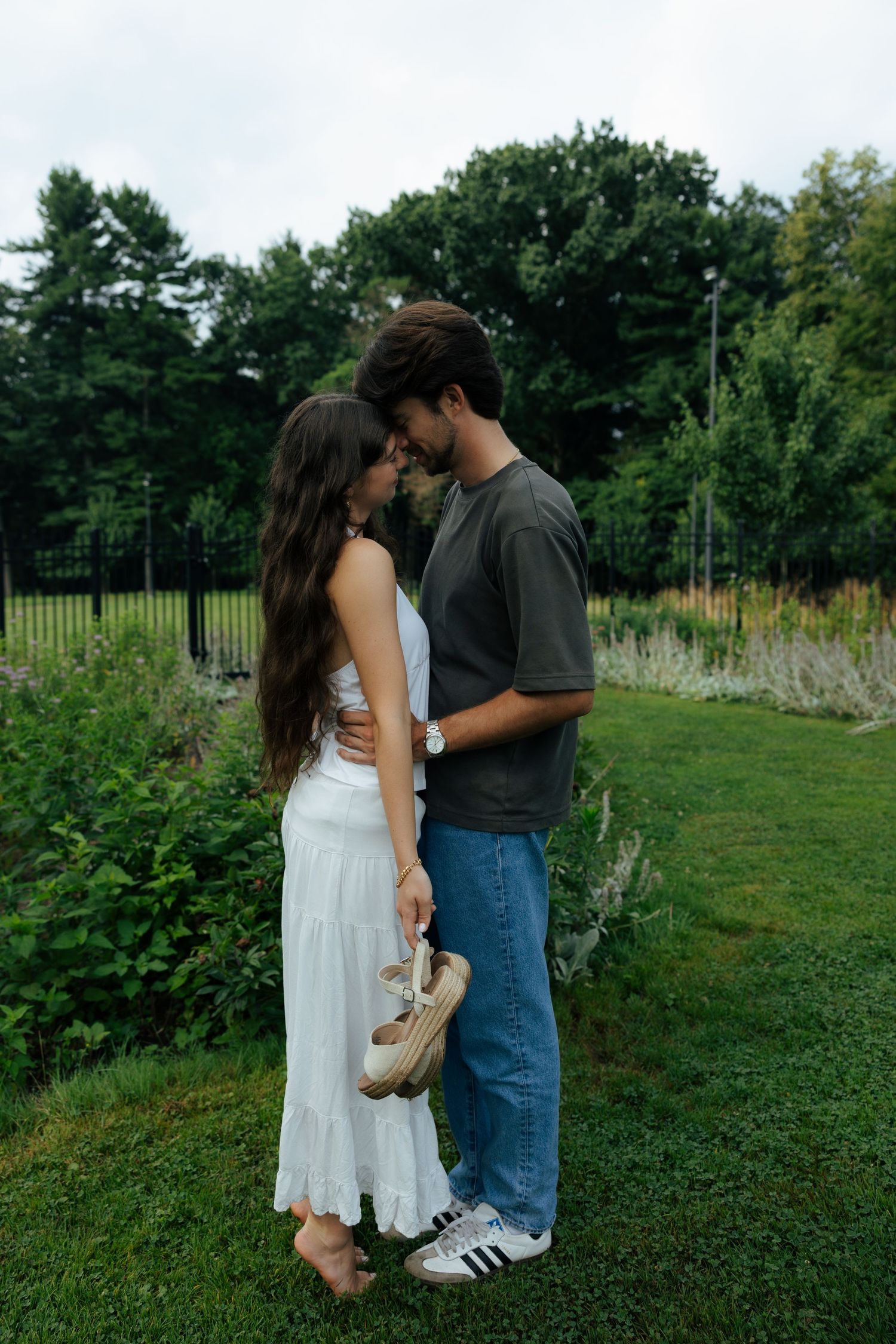 Couple sharing a tender kiss while standing barefoot on green grass in a lush garden.