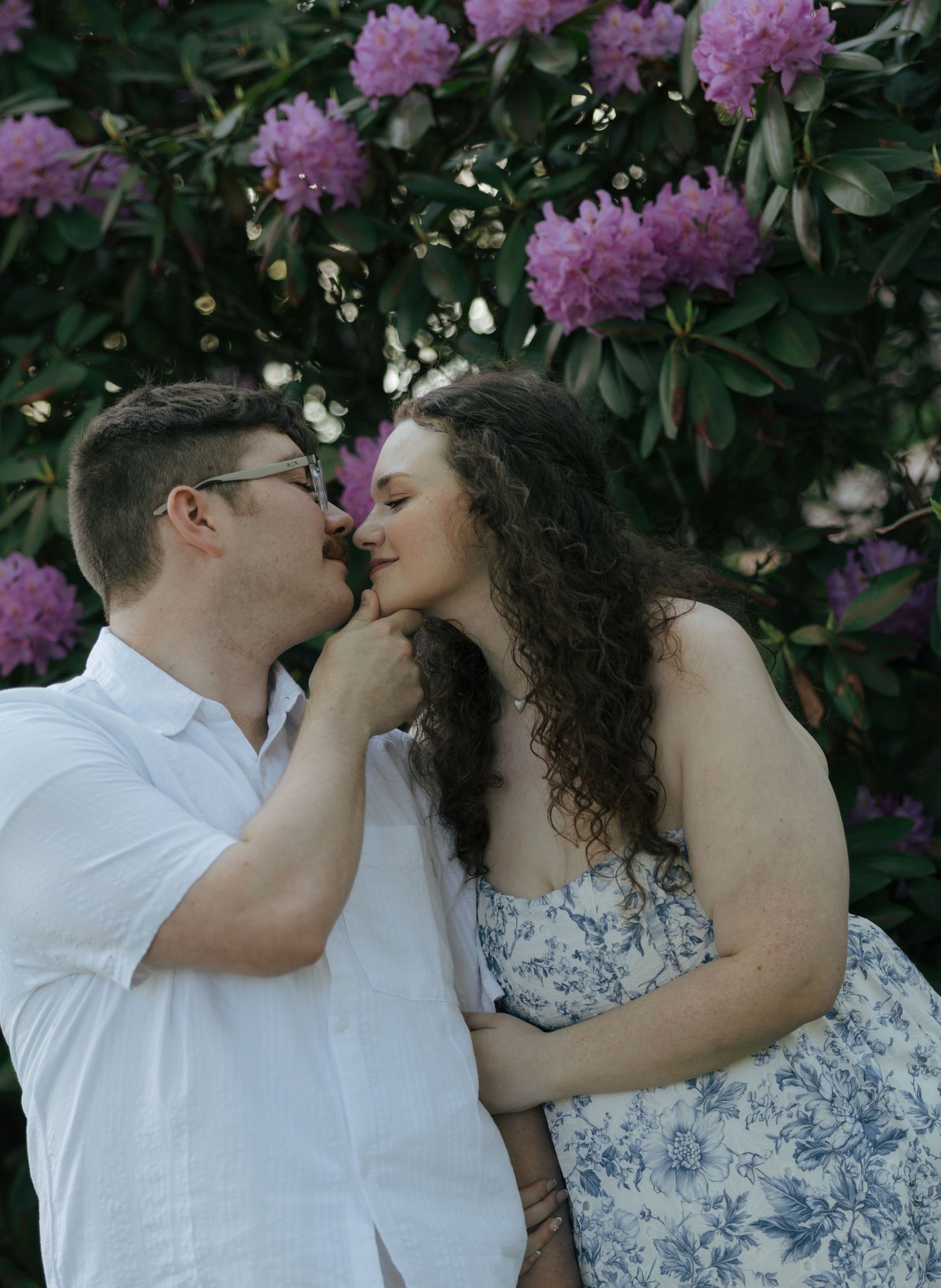 Couple sharing a tender moment in front of vibrant purple rhododendron blooms in a garden.