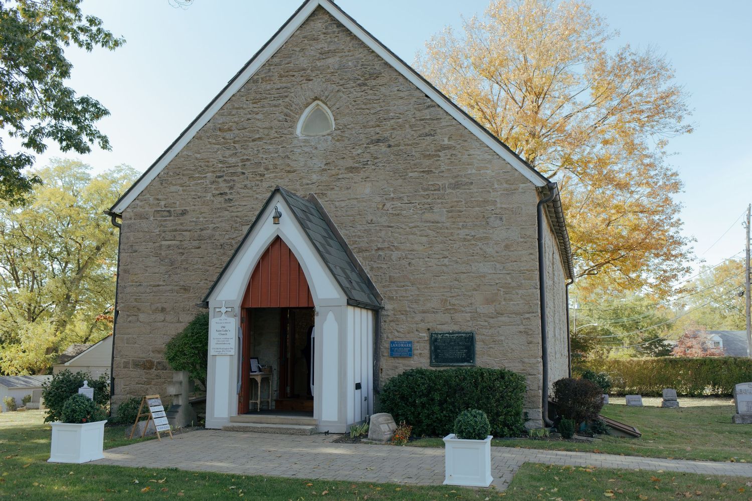 Historic stone church with arched wooden entrance doors, Gothic window, and autumn trees in a serene outdoor setting.