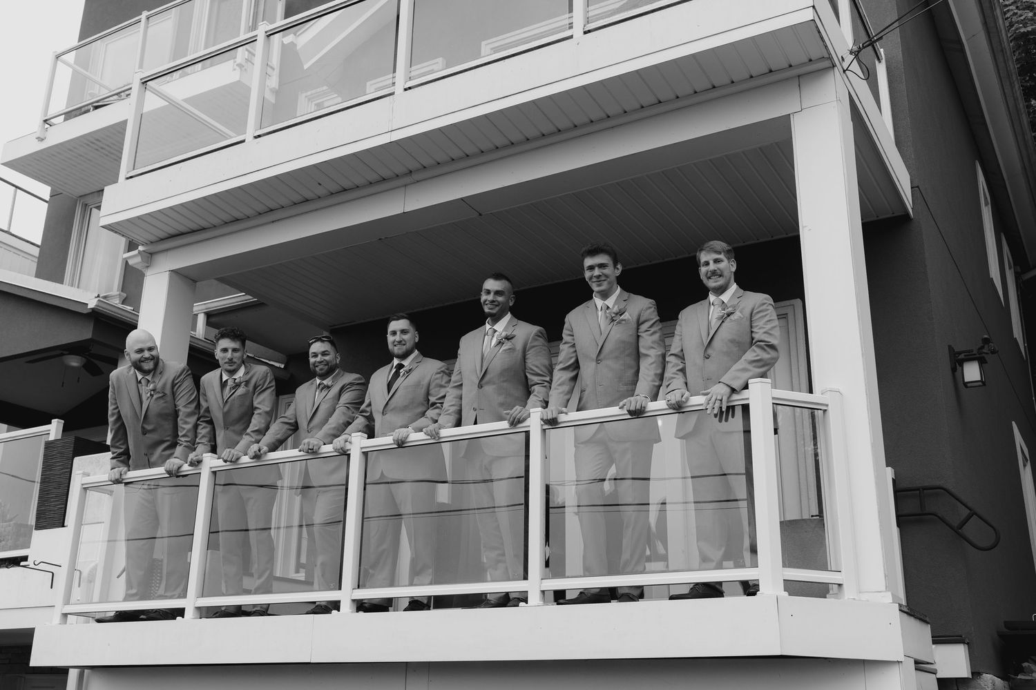 Group of men in suits posing on a balcony of a multi-story building in a black and white photo.